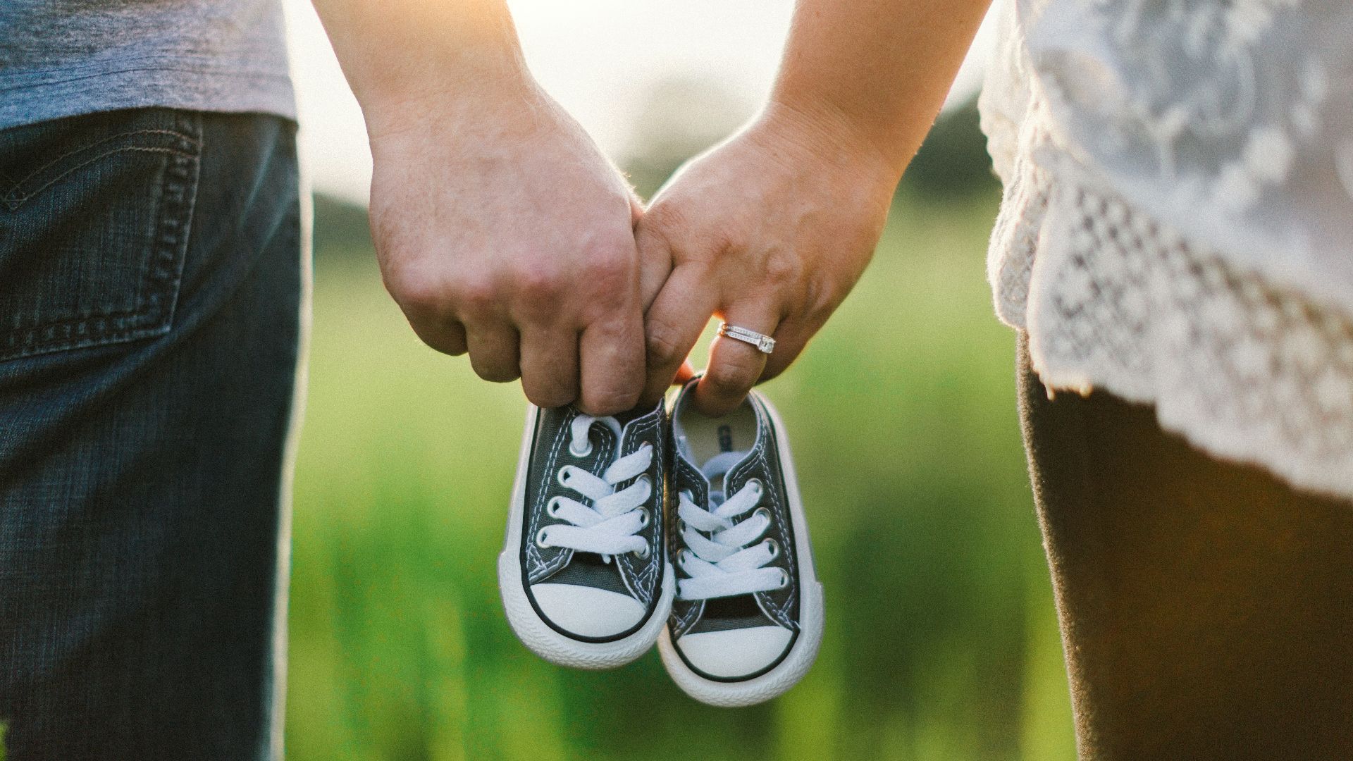 woman and man holding black crib shoes standing near green grass during daytime
