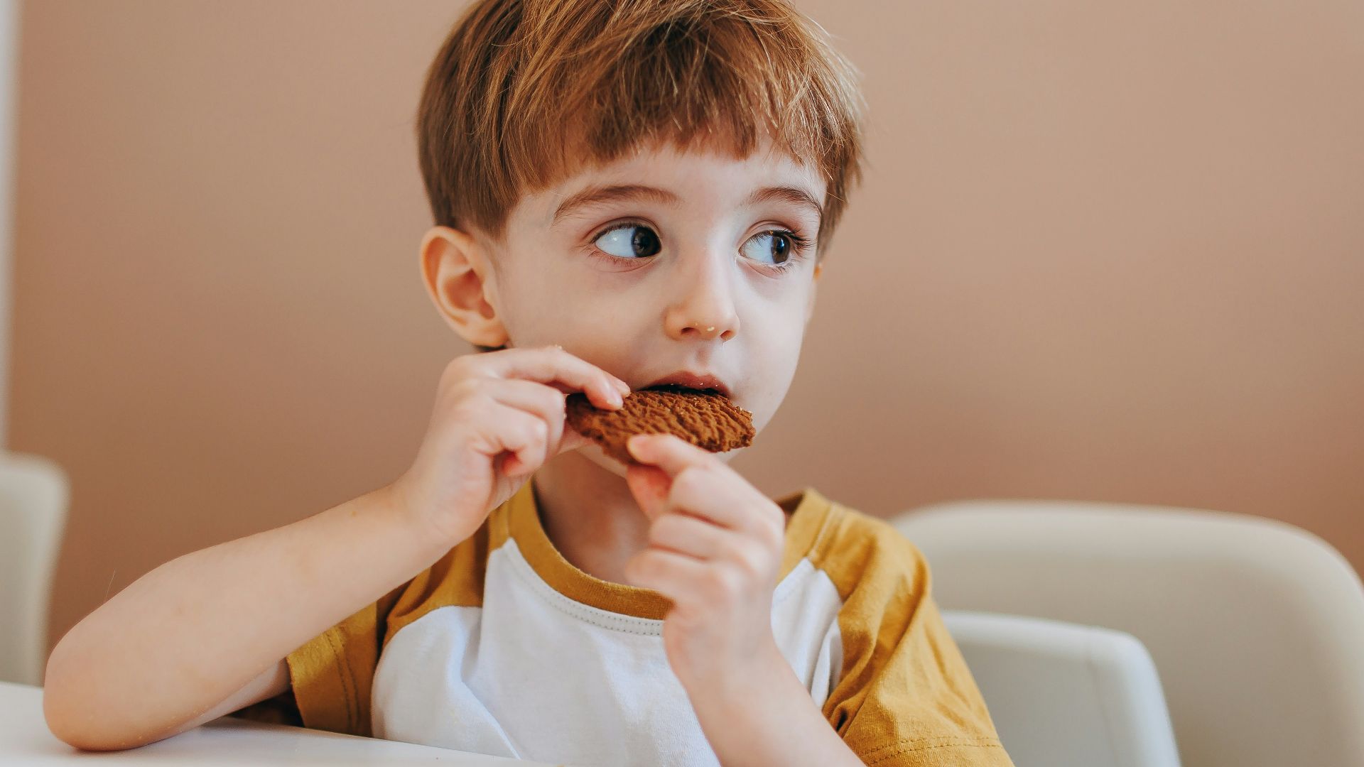 a young boy sitting at a table eating a chocolate donut