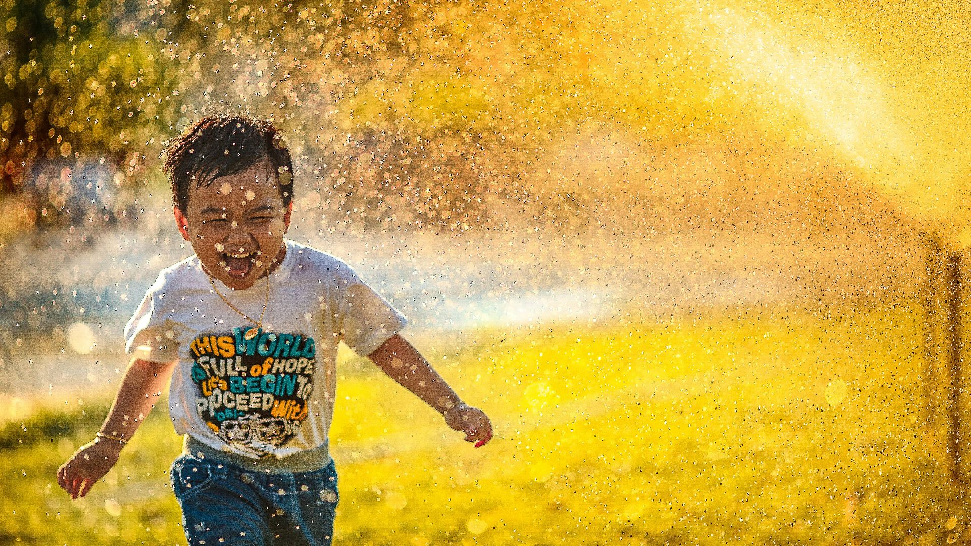 a young boy running through a sprinkle of water