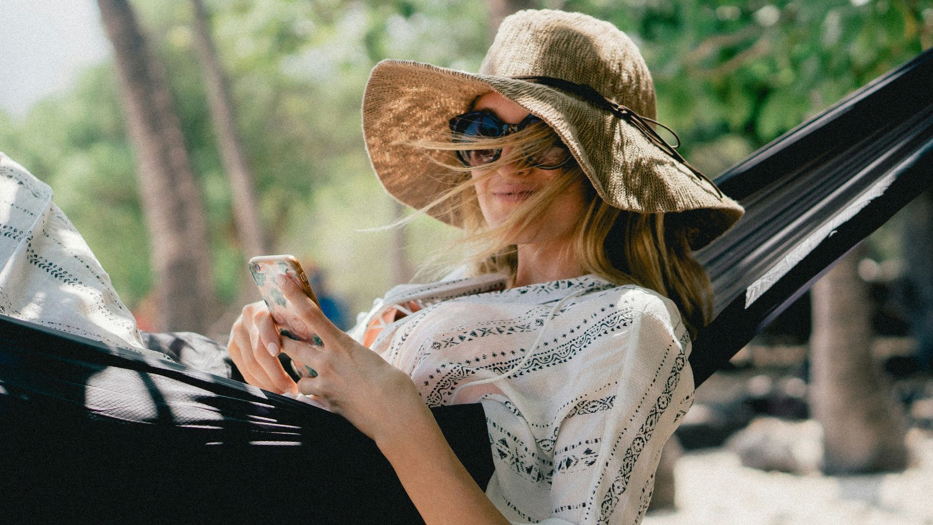 woman lying on black hammock while holding phone
