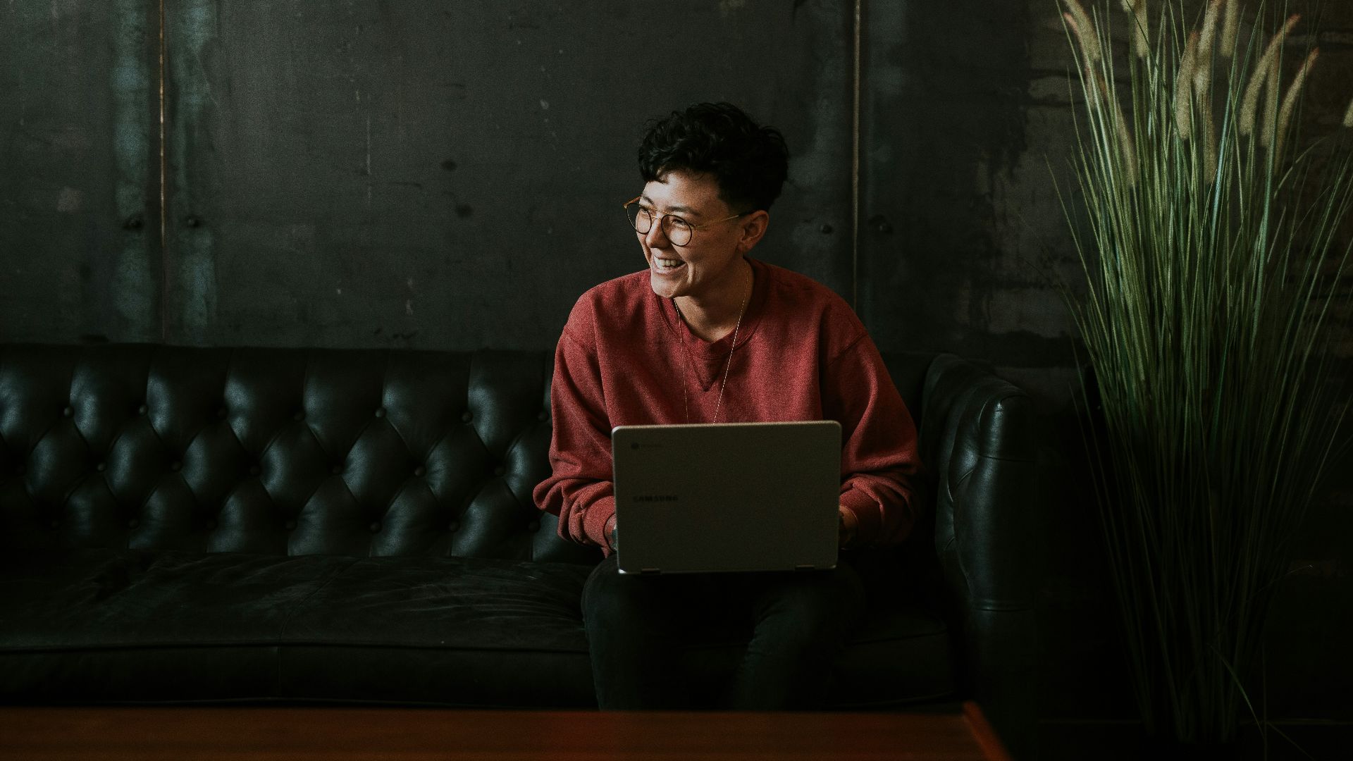 smiling man using laptop computer while sitting on black leather sofa