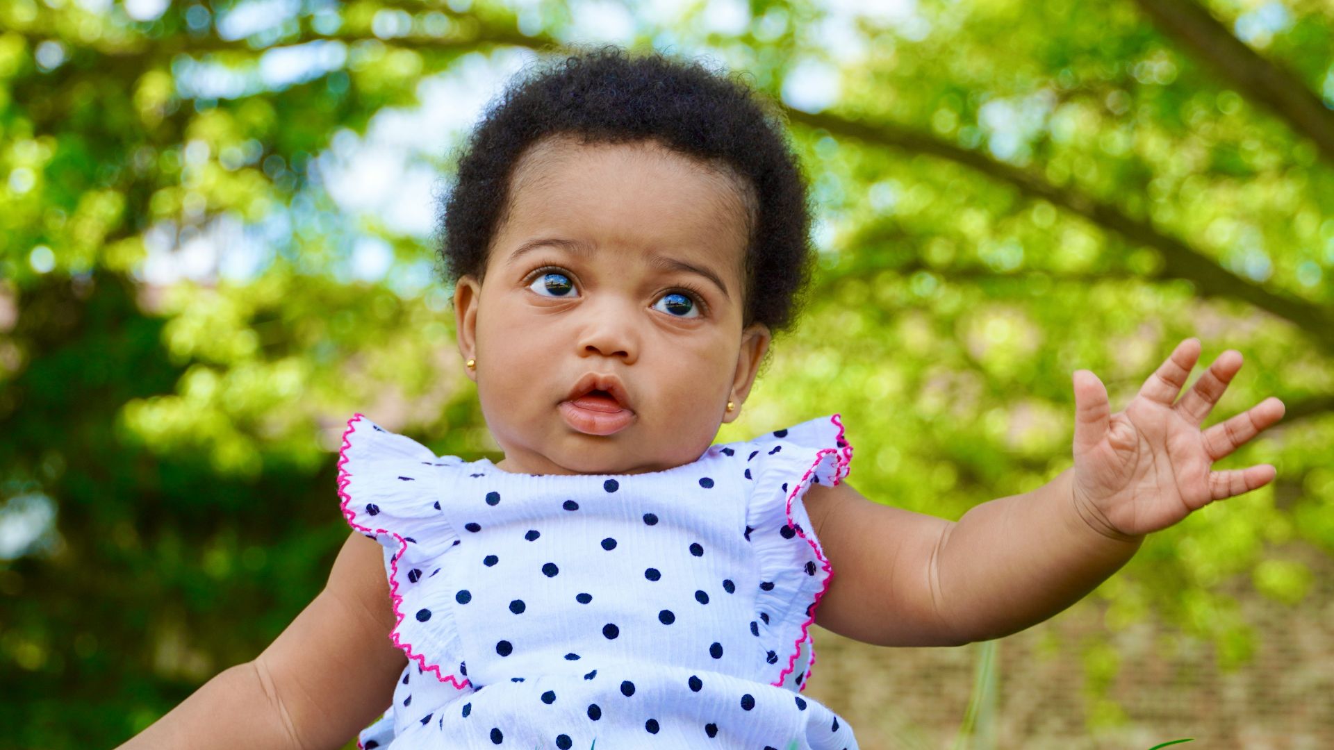 a baby girl sitting in the grass with her hands out