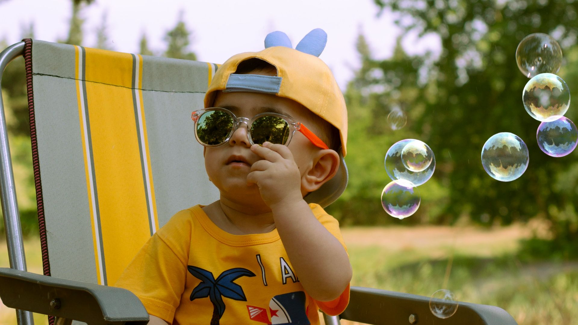 a little boy sitting in a lawn chair blowing bubbles