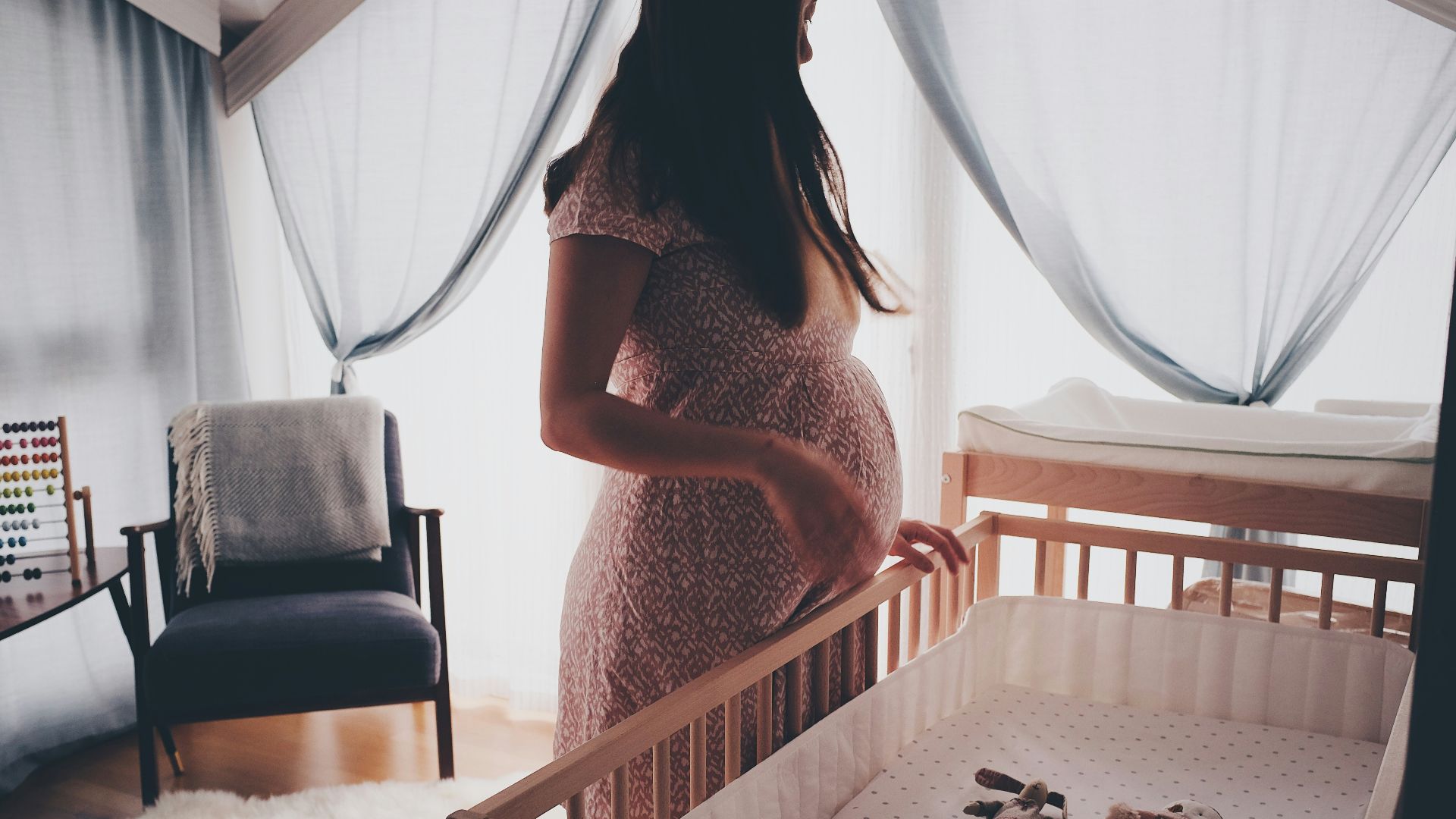 woman in white lace sleeveless dress standing beside brown wooden crib