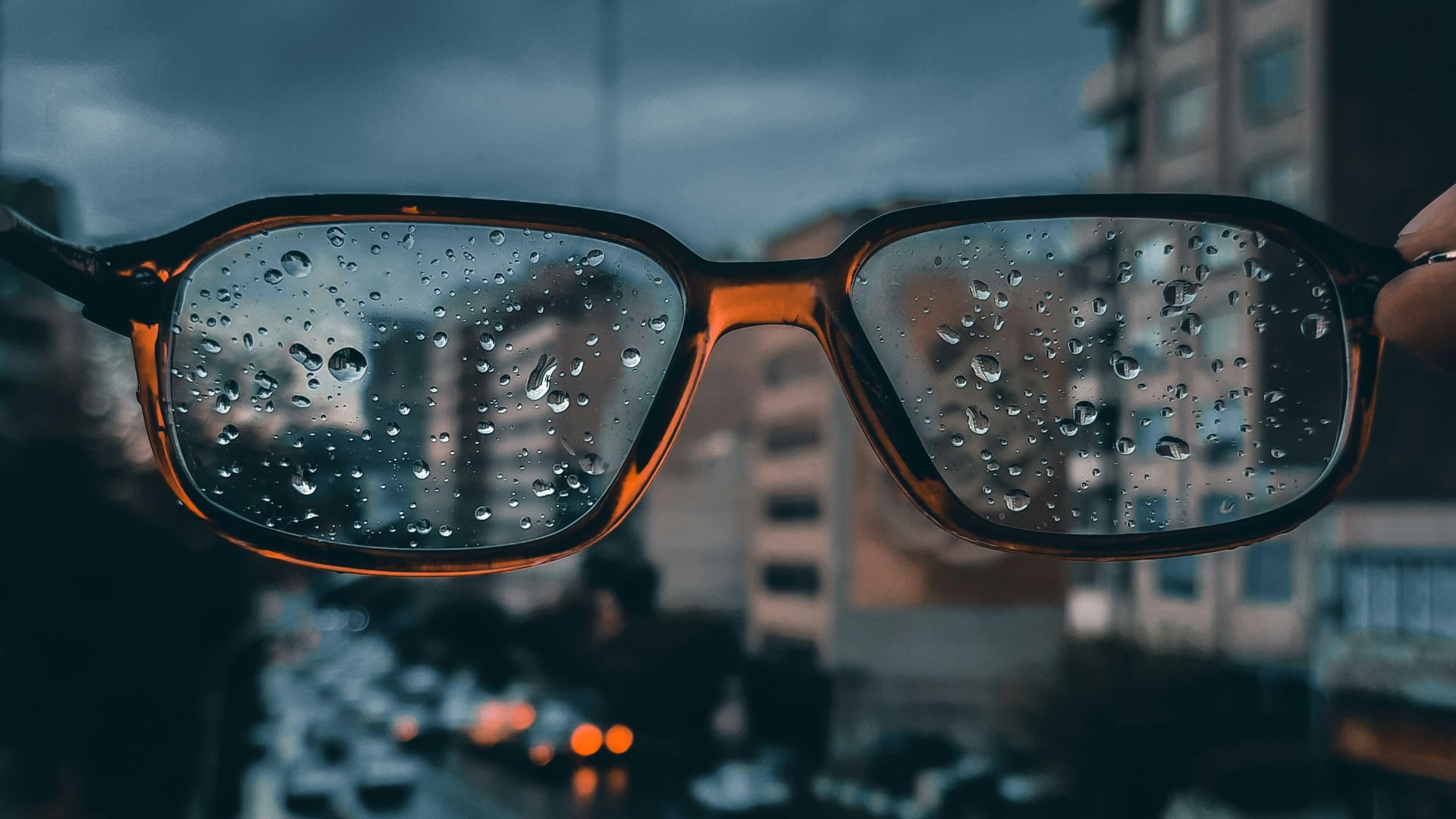 a person holding up a pair of glasses with rain drops on them