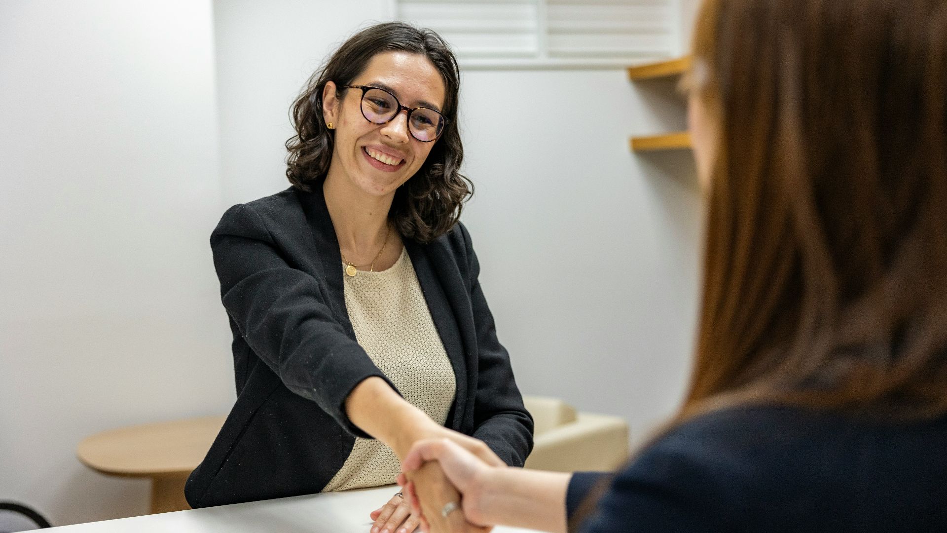 a woman shaking hands with another woman sitting at a table
