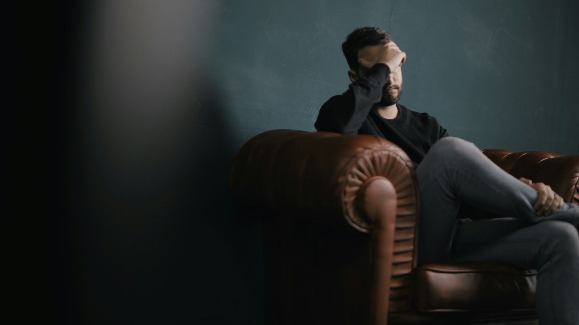 a man holds his head while sitting on a sofa