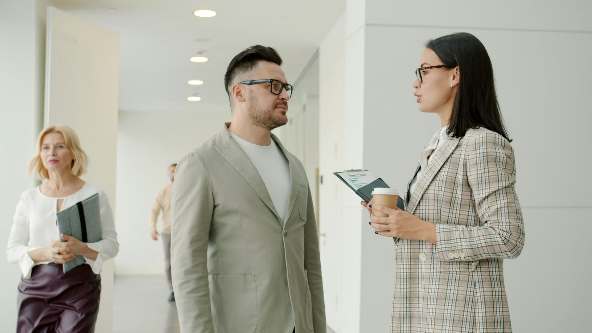Two colleagues talking in a modern office hallway.