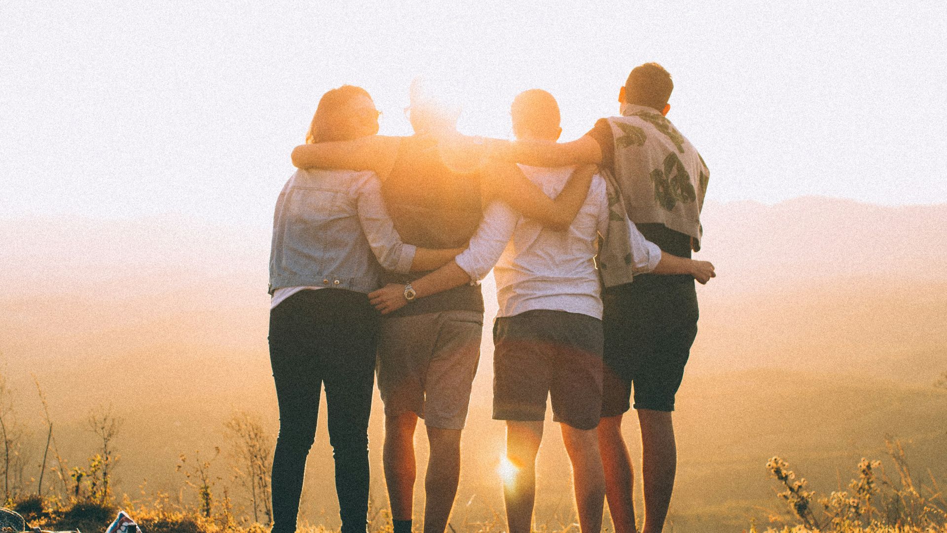 four person hands wrap around shoulders while looking at sunset