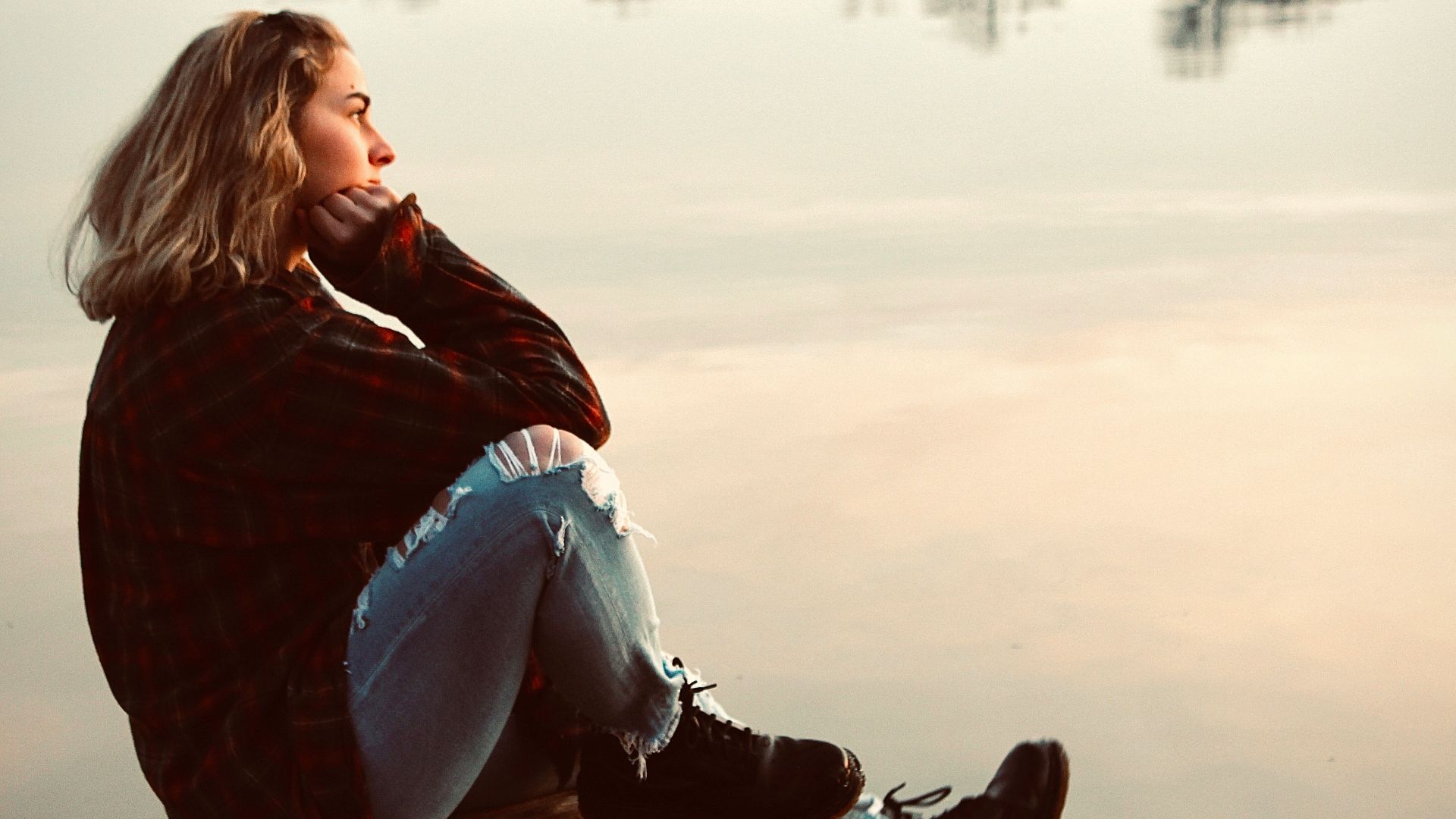 woman in black and red plaid long sleeve shirt and white pants sitting on brown wooden