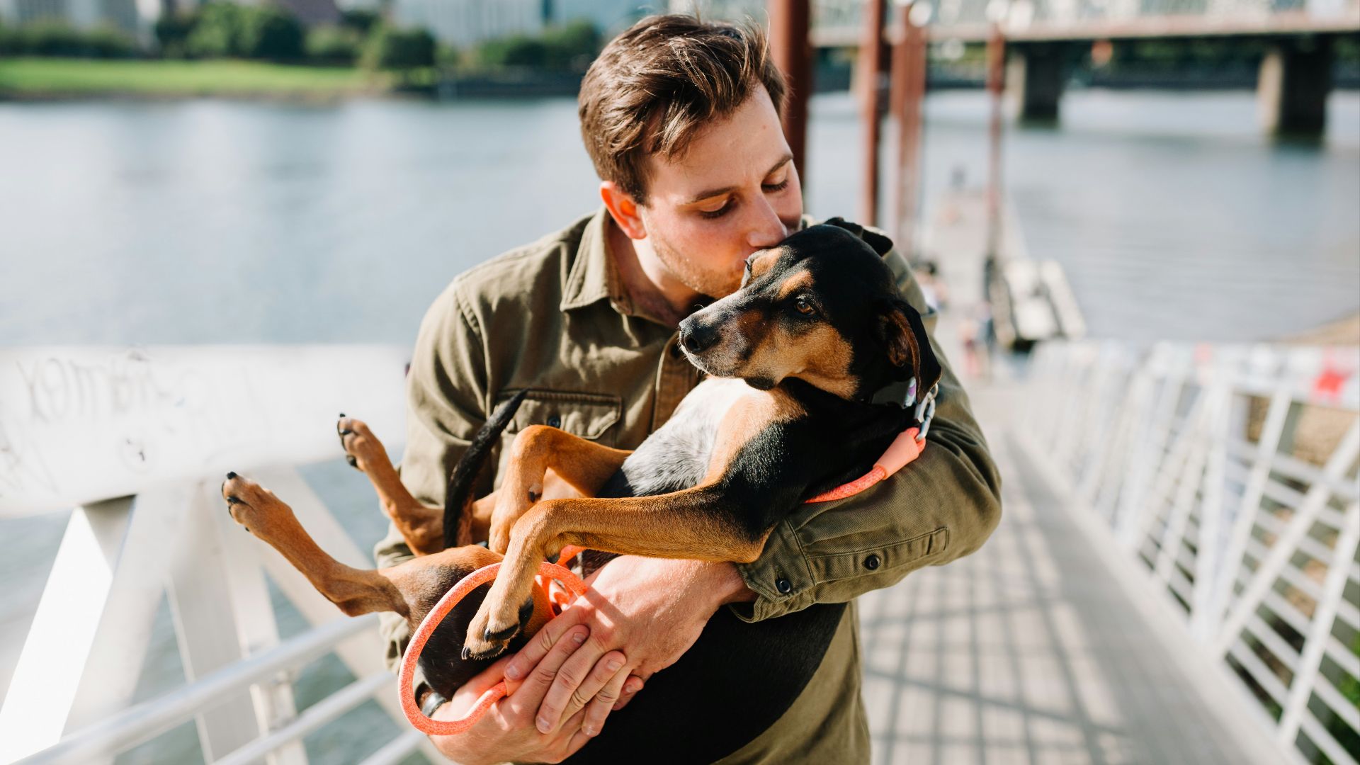 man in brown jacket hugging black and brown short coated dog