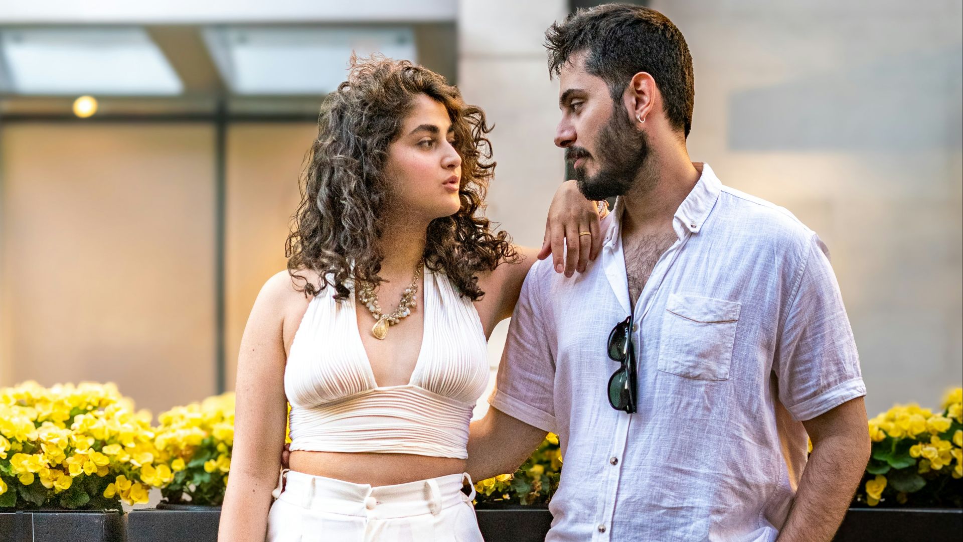 A couple poses together outdoors, looking at each other.