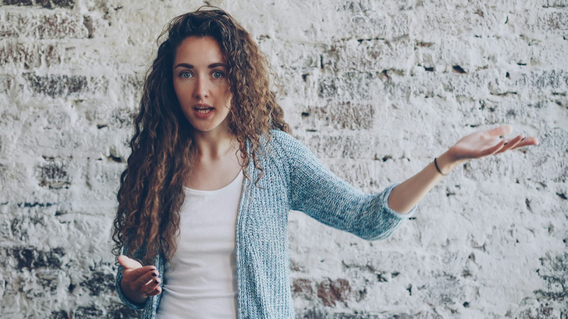 Woman gesturing while speaking against brick wall.