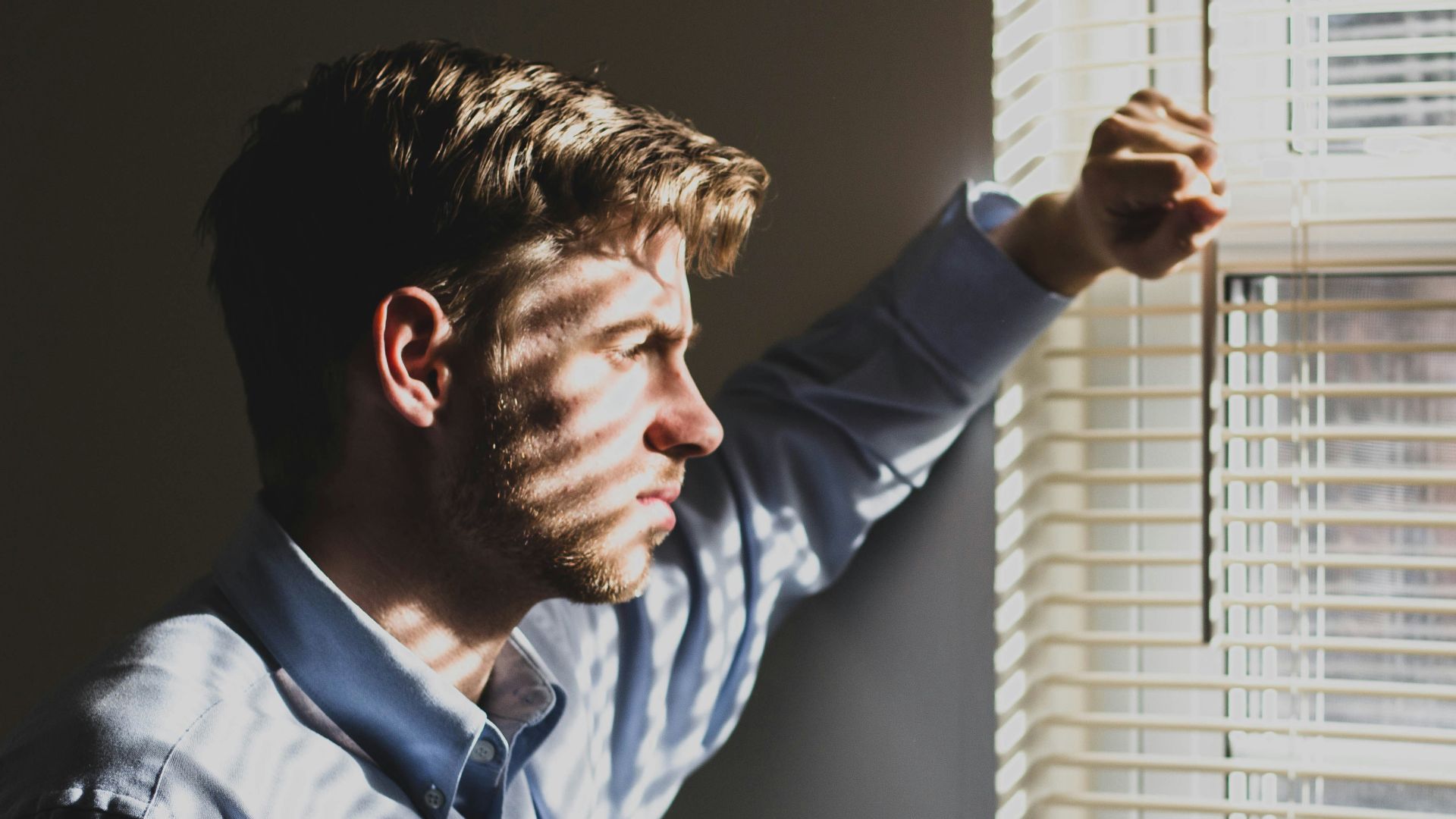 person near clear glass window pane and window blinds low-light photography