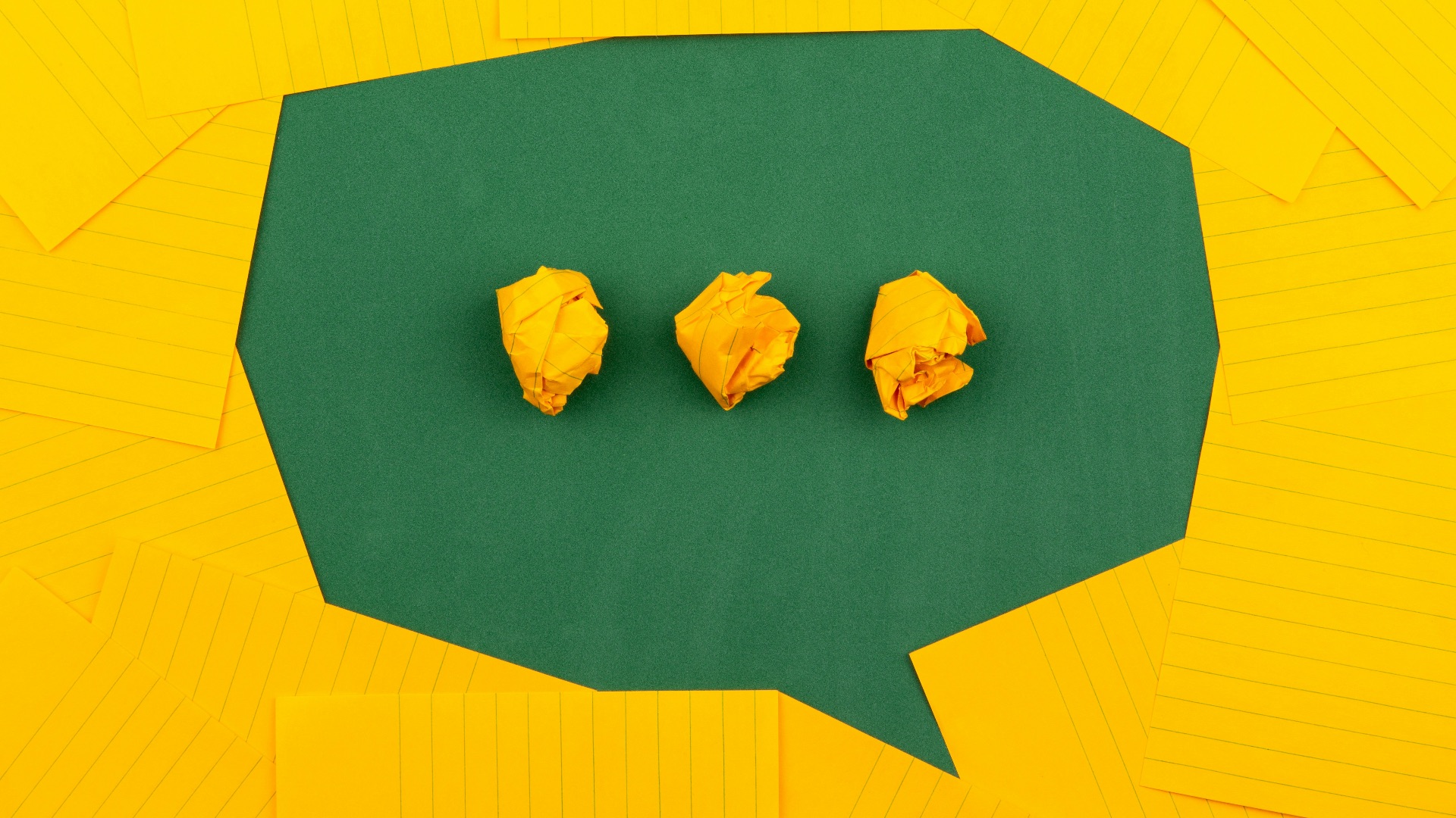 three crumpled yellow papers on green surface surrounded by yellow lined papers