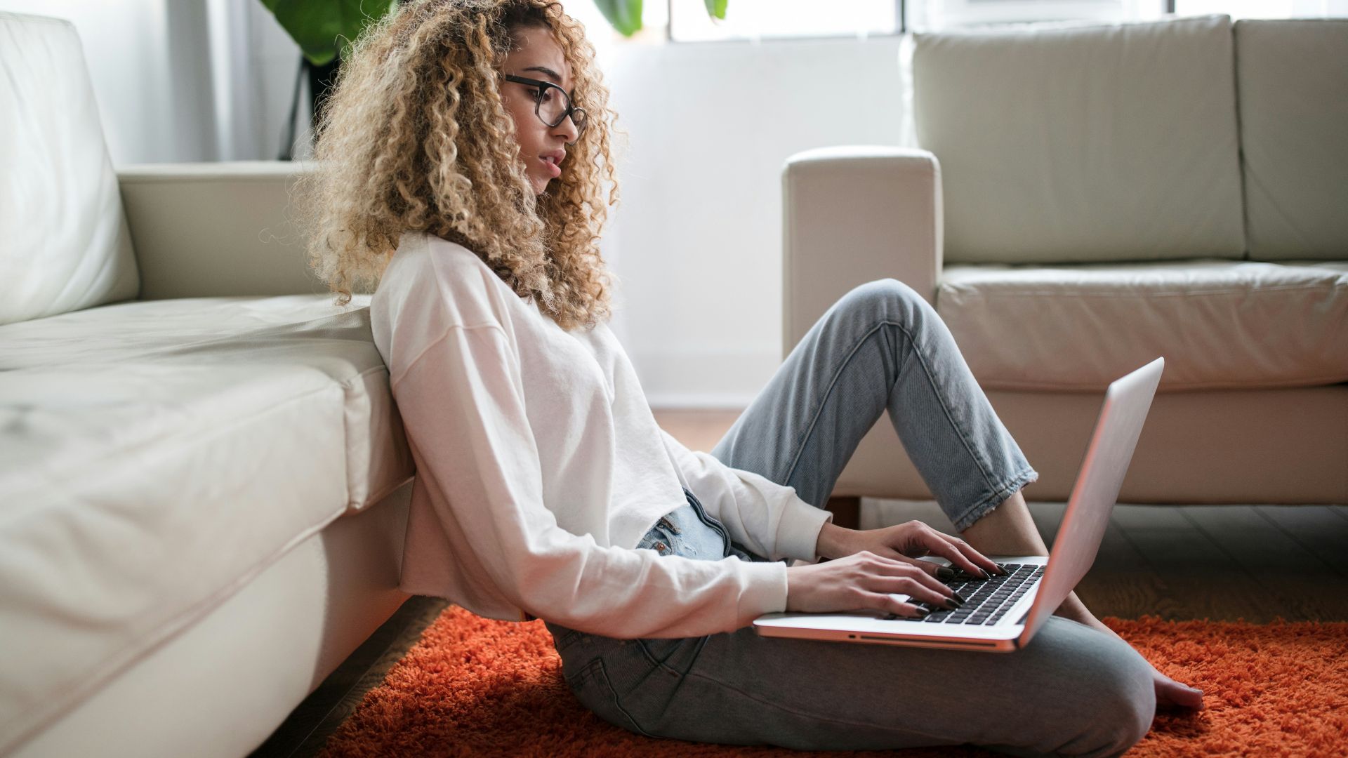 woman sitting on floor and leaning on couch using laptop