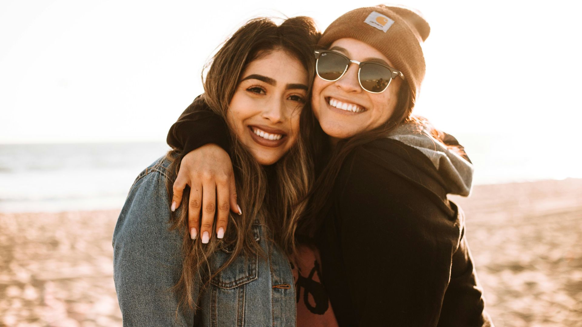 woman hugging other woman while smiling at beach