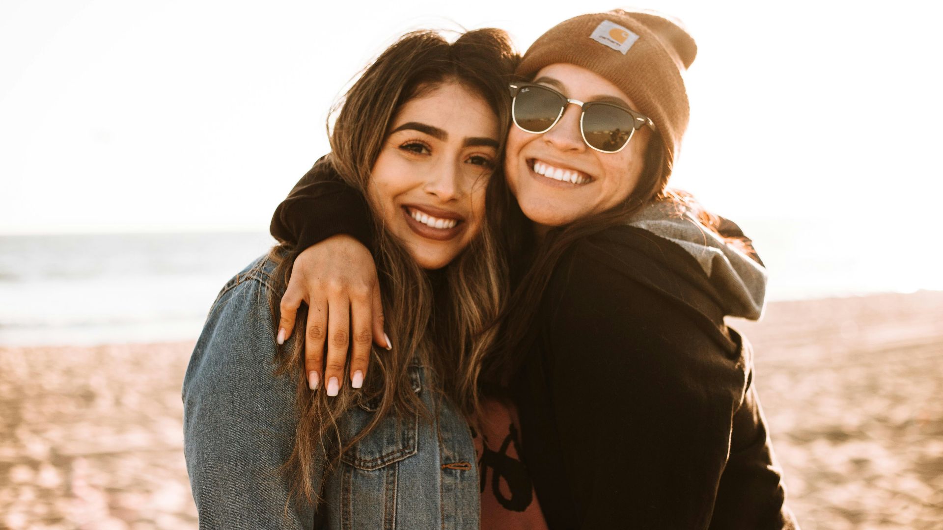 woman hugging other woman while smiling at beach