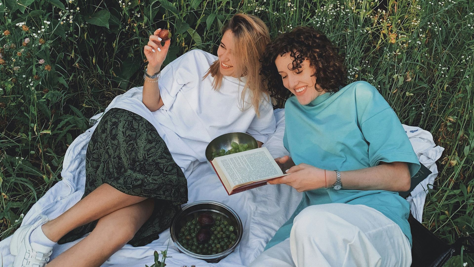 man and woman sitting on white bed reading book