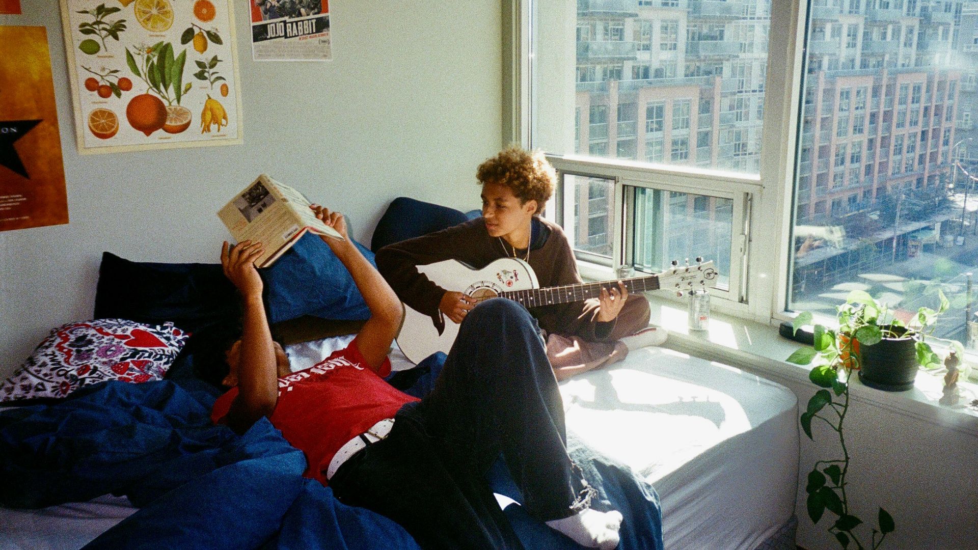 a young man sitting on a bed reading a book