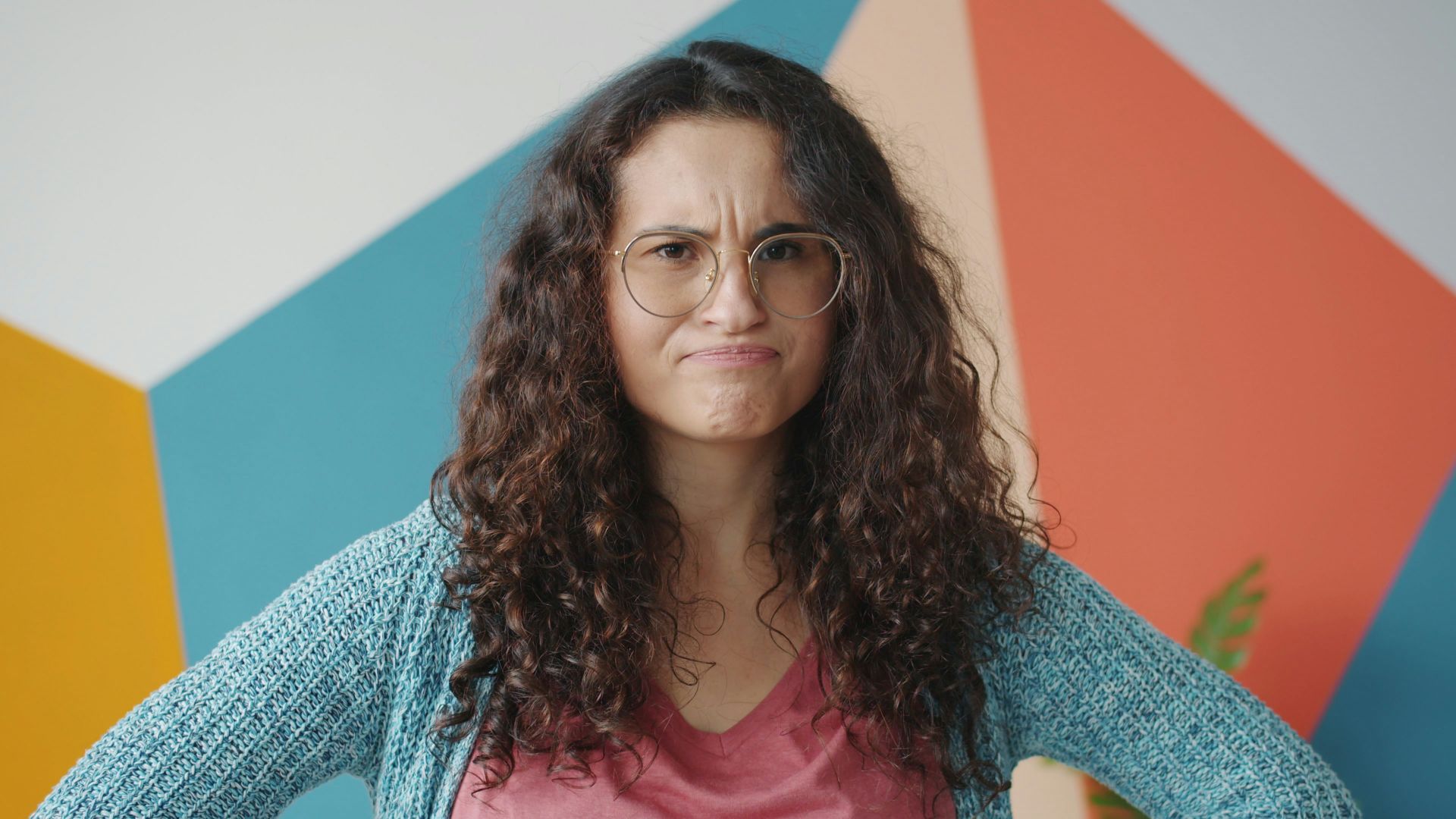Woman with curly hair and glasses looks annoyed.