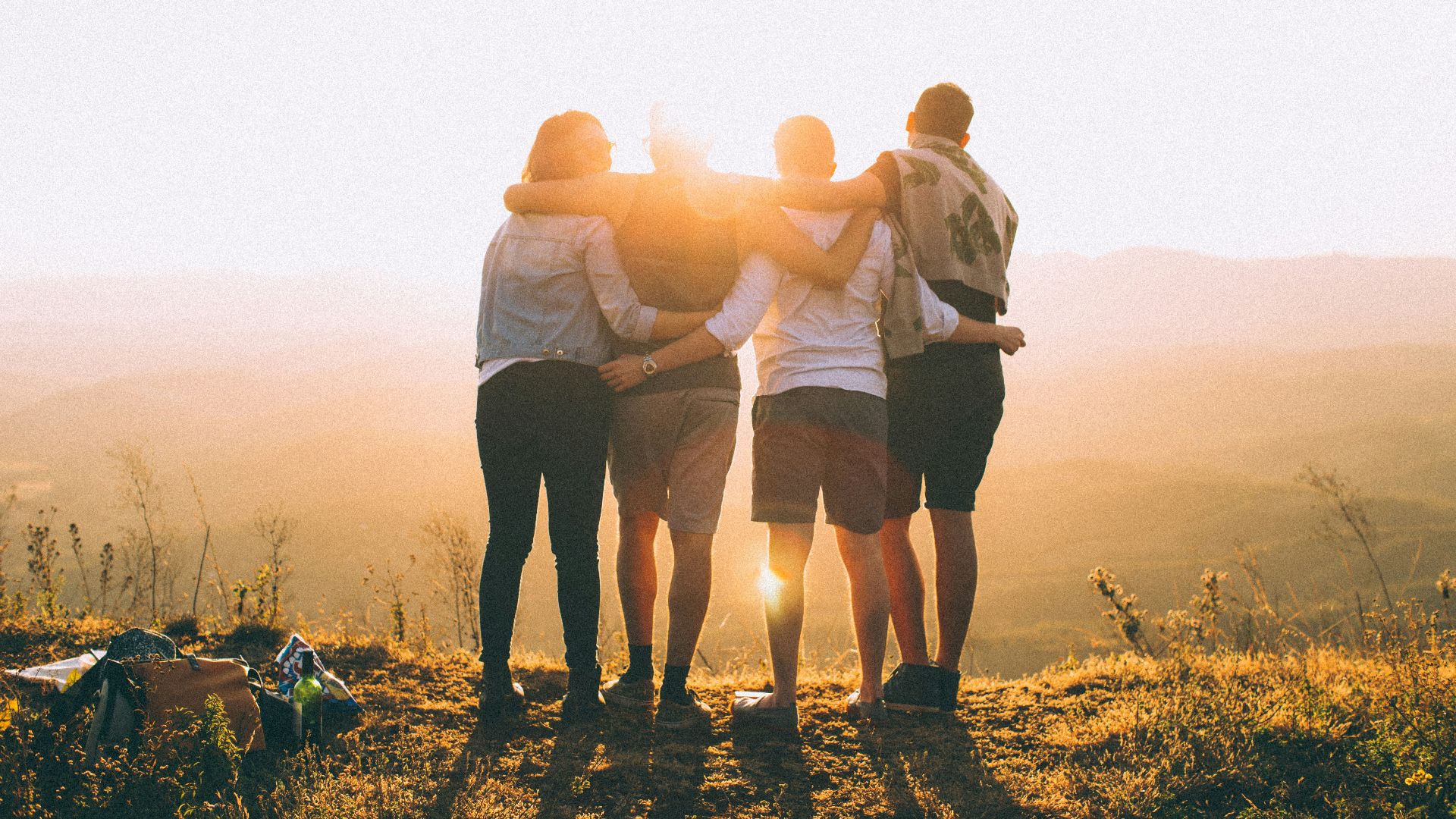 four person hands wrap around shoulders while looking at sunset