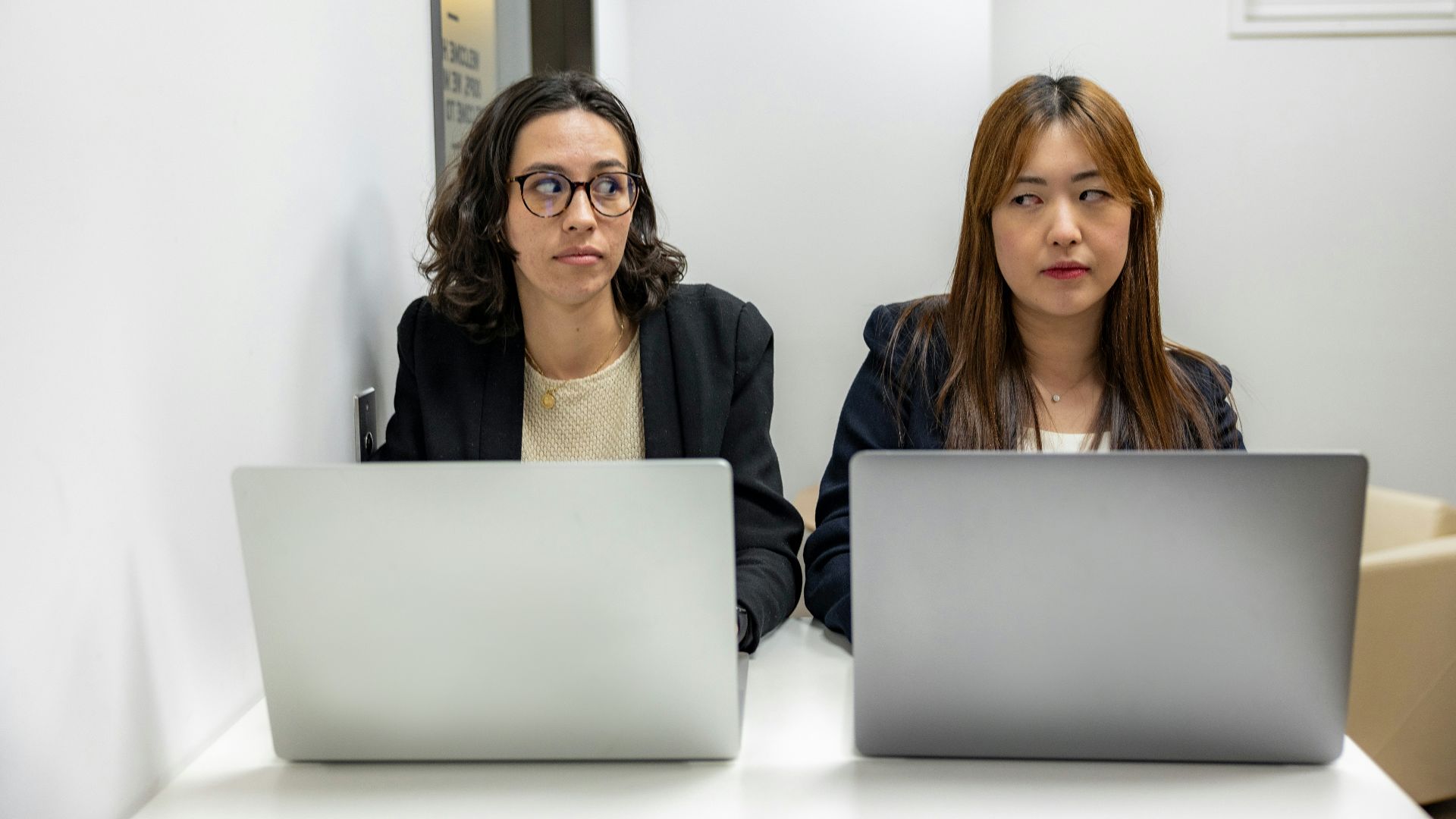 two women sitting at a table with laptops