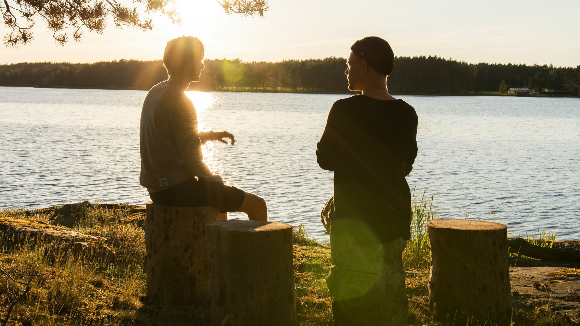 man in black jacket standing beside body of water during sunset