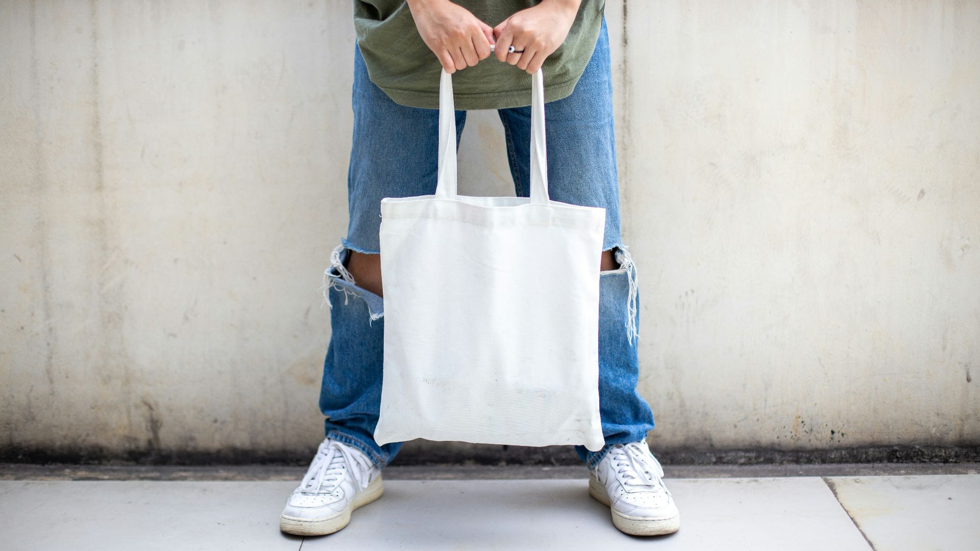 person in blue denim jeans holding white tote bag