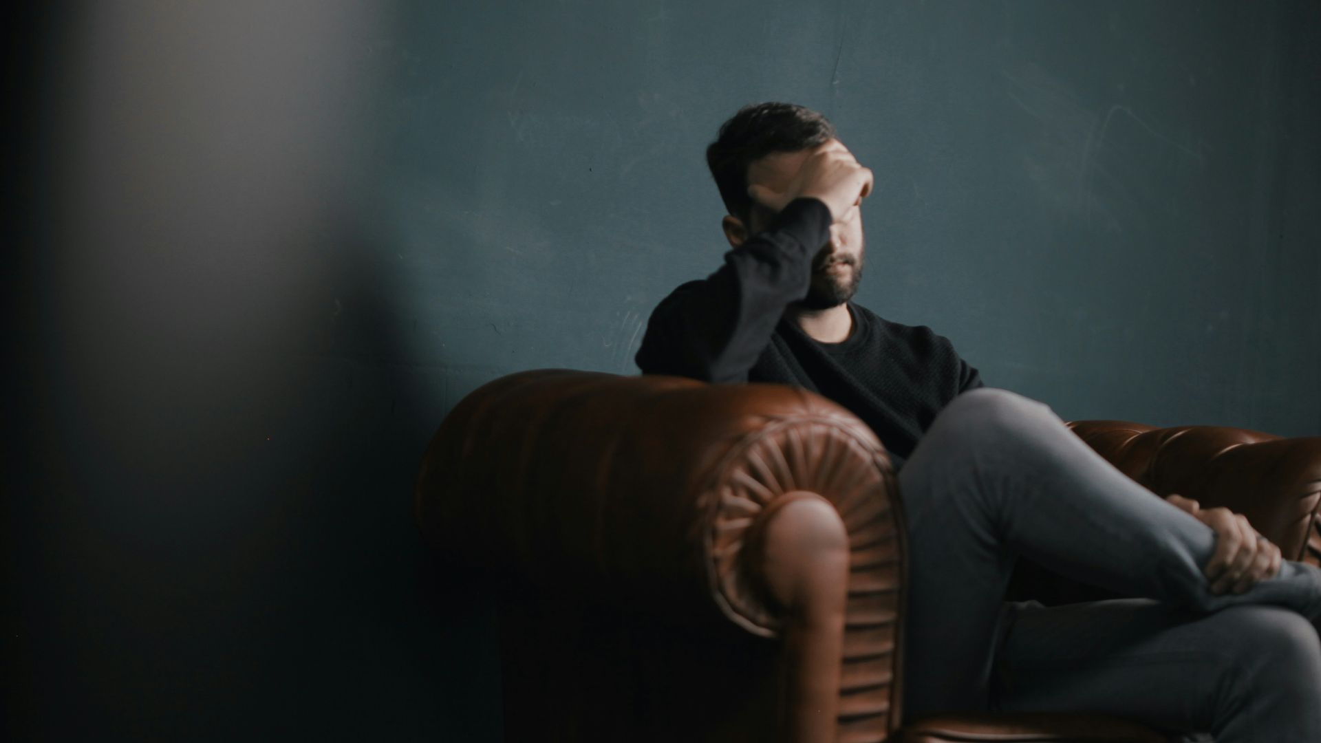 a man holds his head while sitting on a sofa