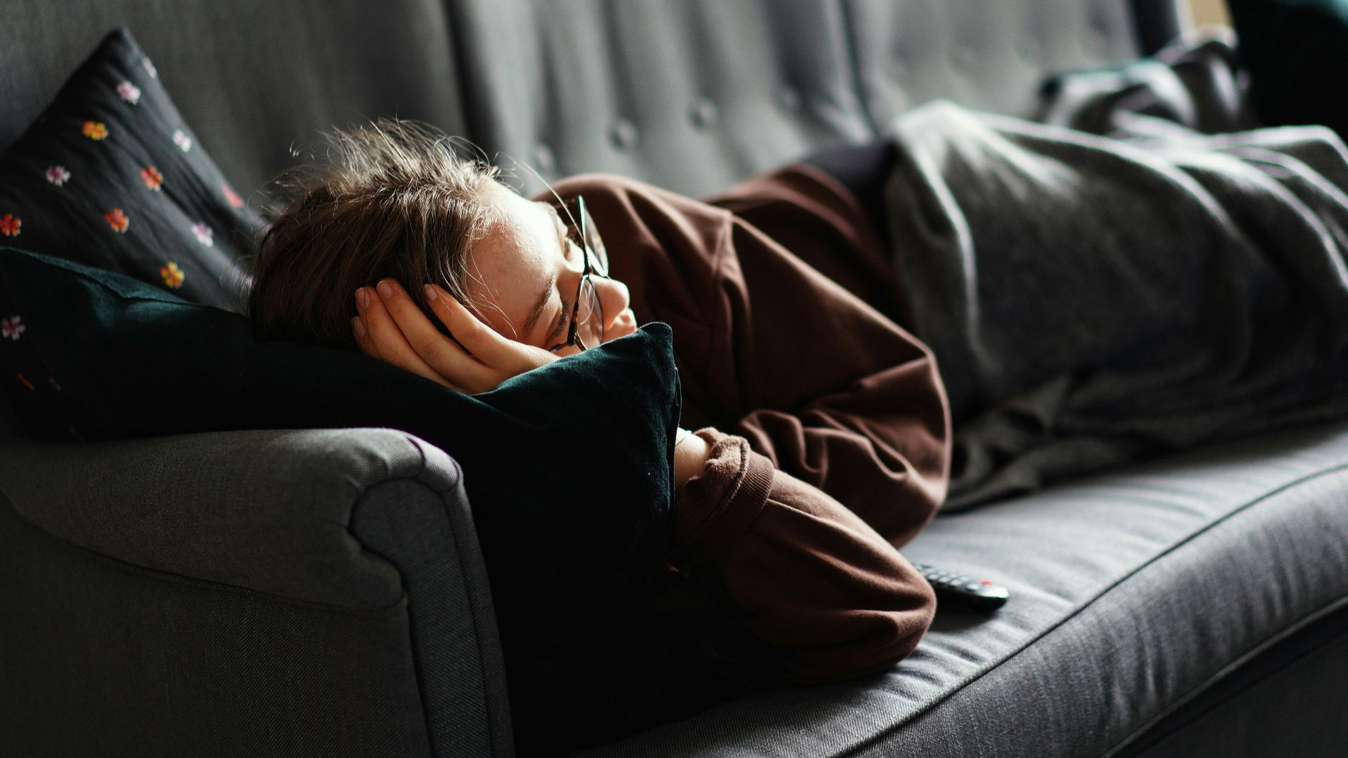 woman in pink jacket lying on gray couch