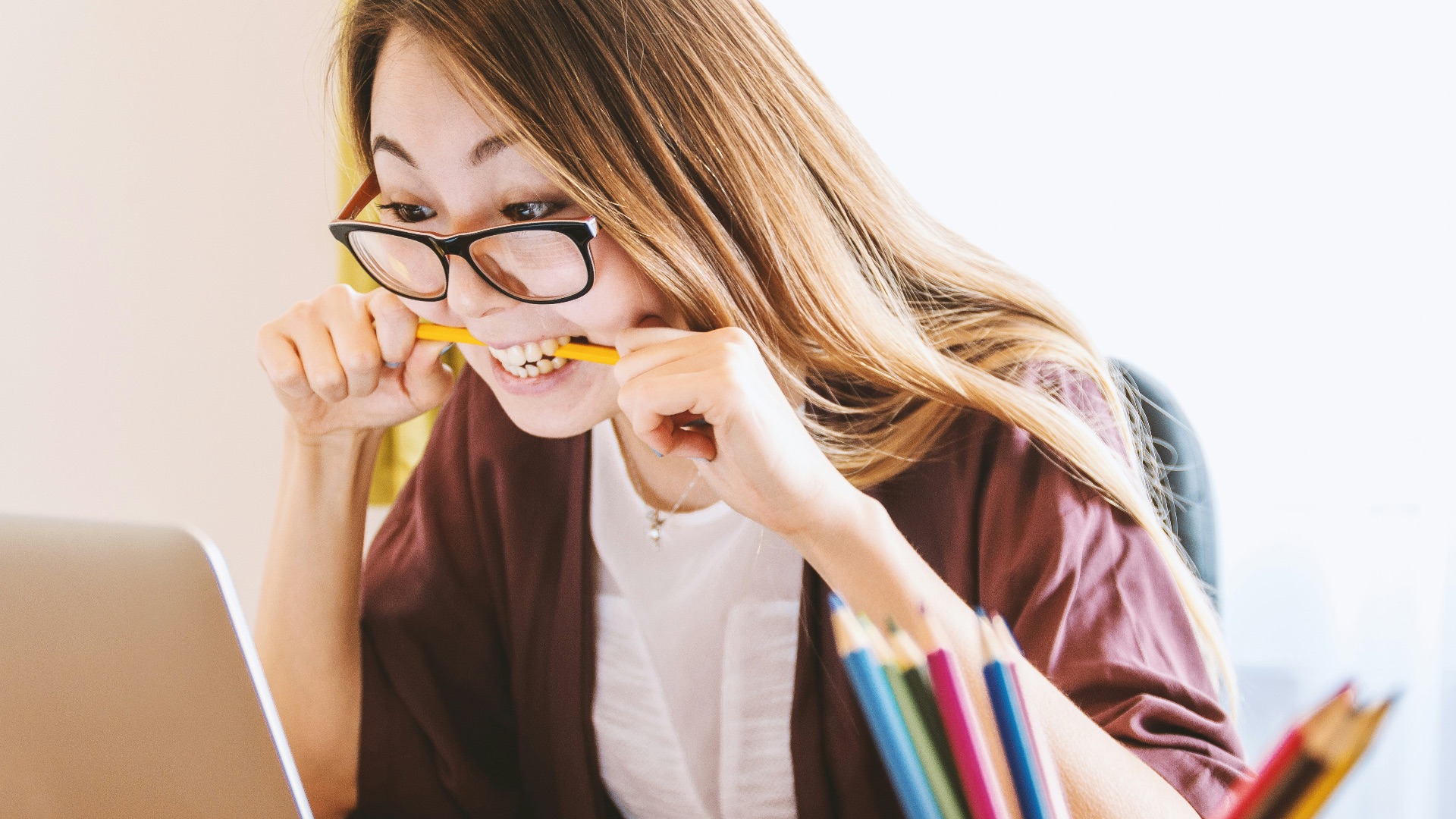woman biting pencil while sitting on chair in front of computer during daytime