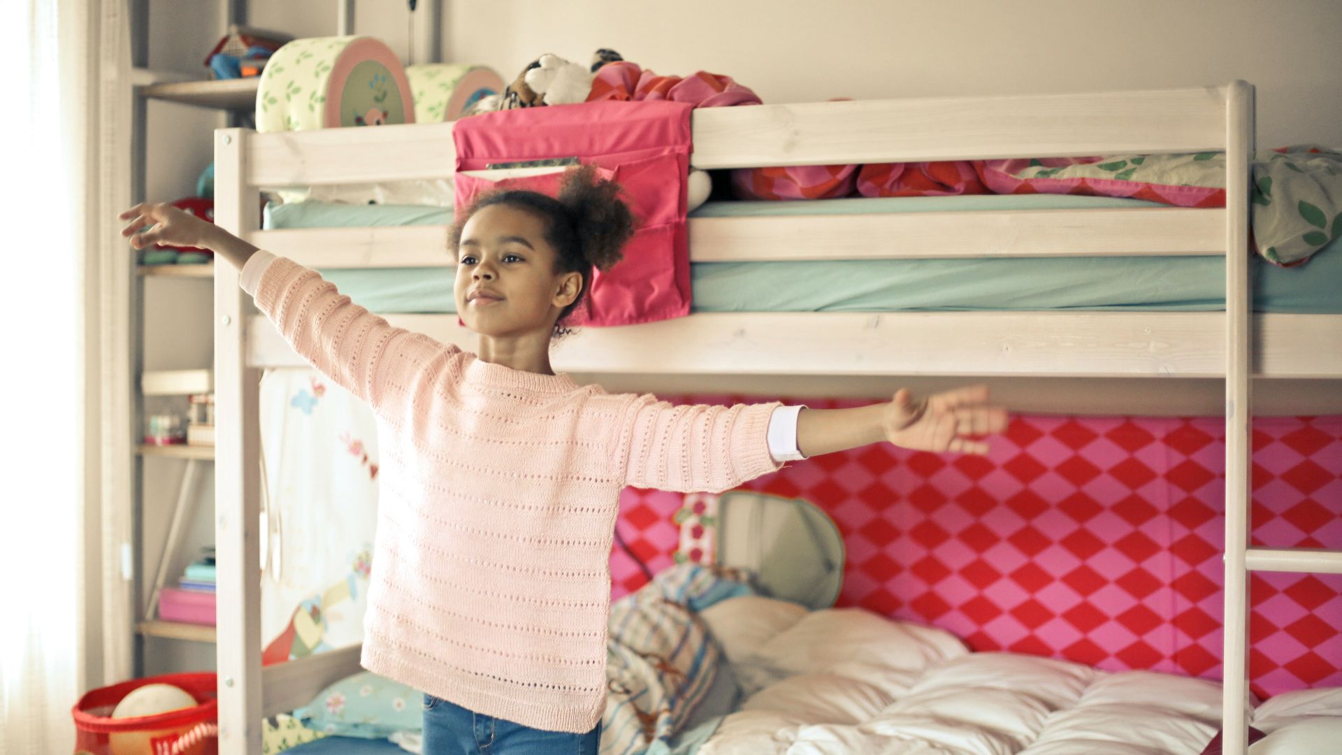girl in white and red long sleeve shirt and blue denim jeans standing near bed