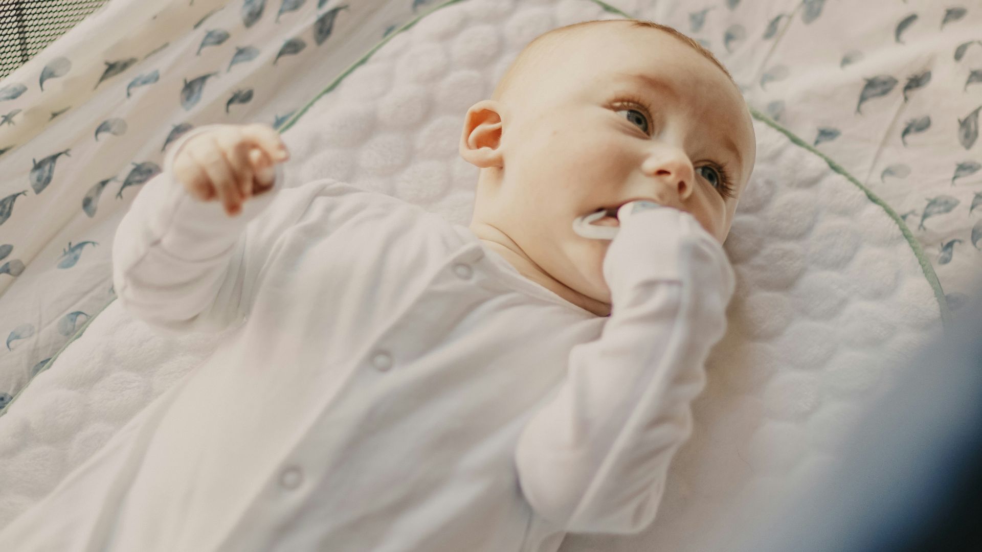 baby in white onesie lying on white and blue bed