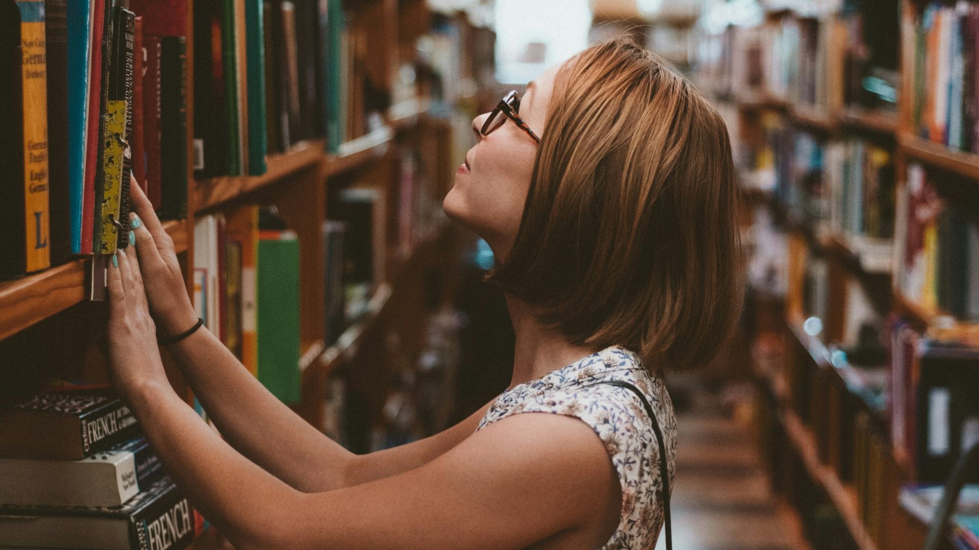woman standing between library book shelves