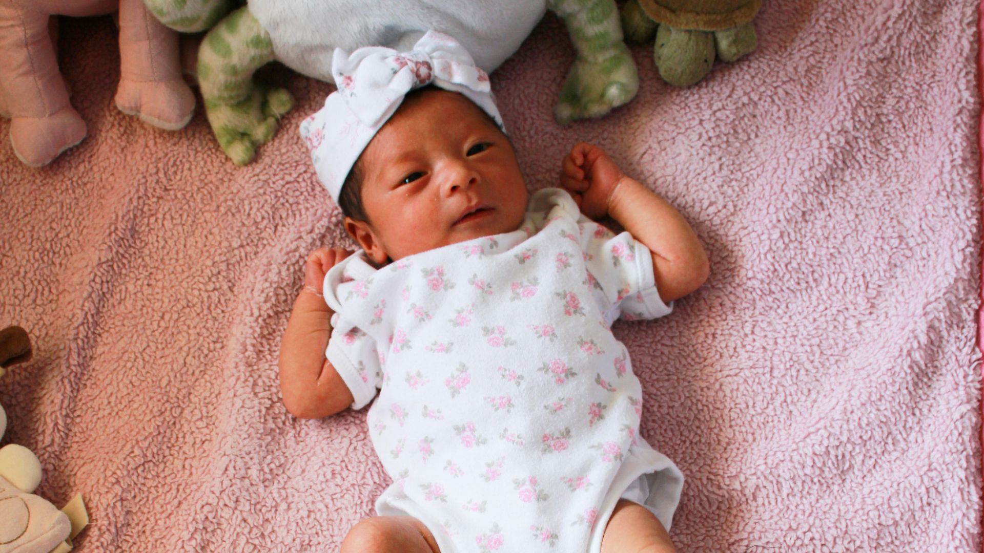 baby in white and pink floral dress lying on pink textile