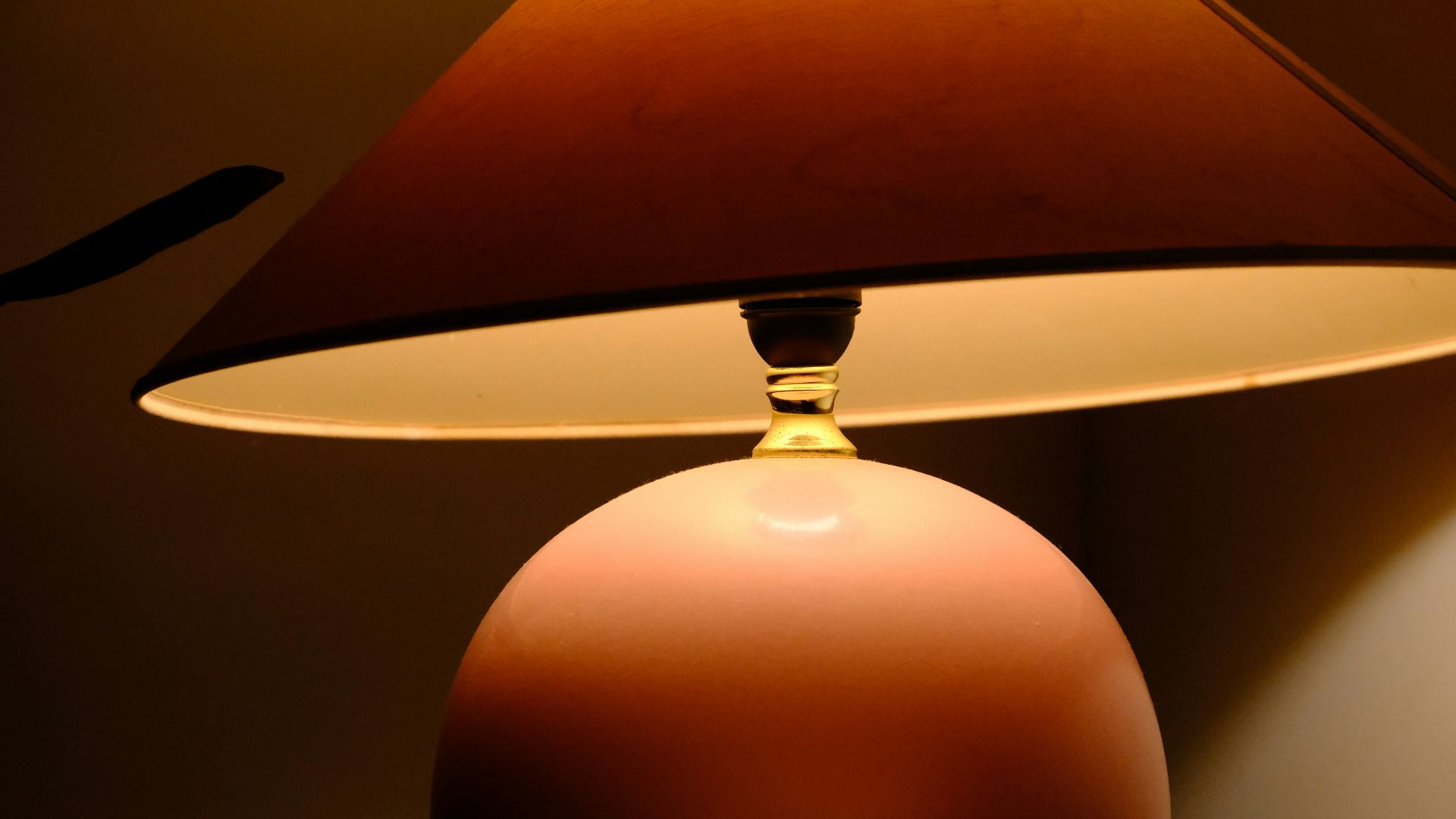 A pink lamp with a brown lampshade glows warmly.