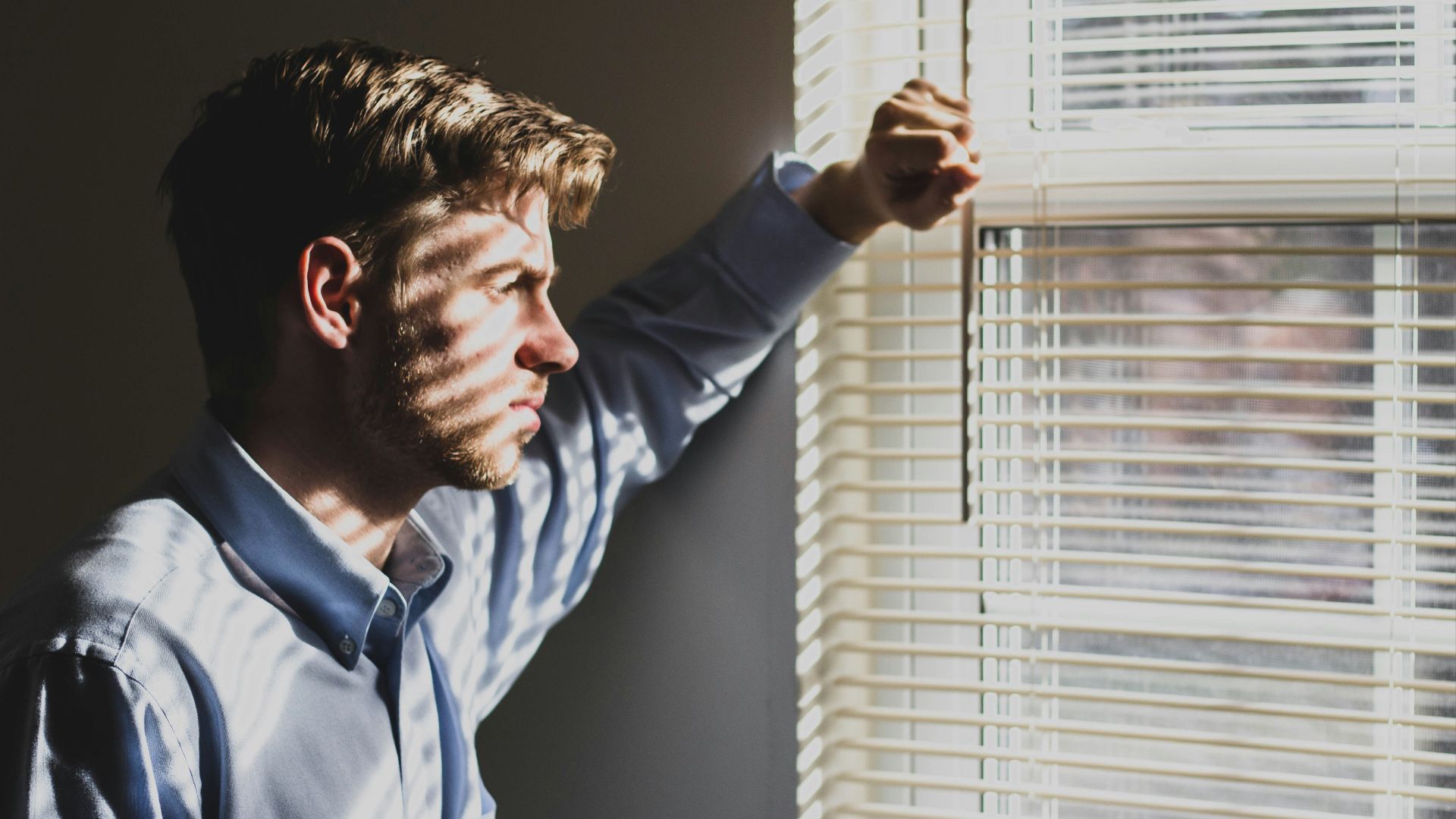 person near clear glass window pane and window blinds low-light photography