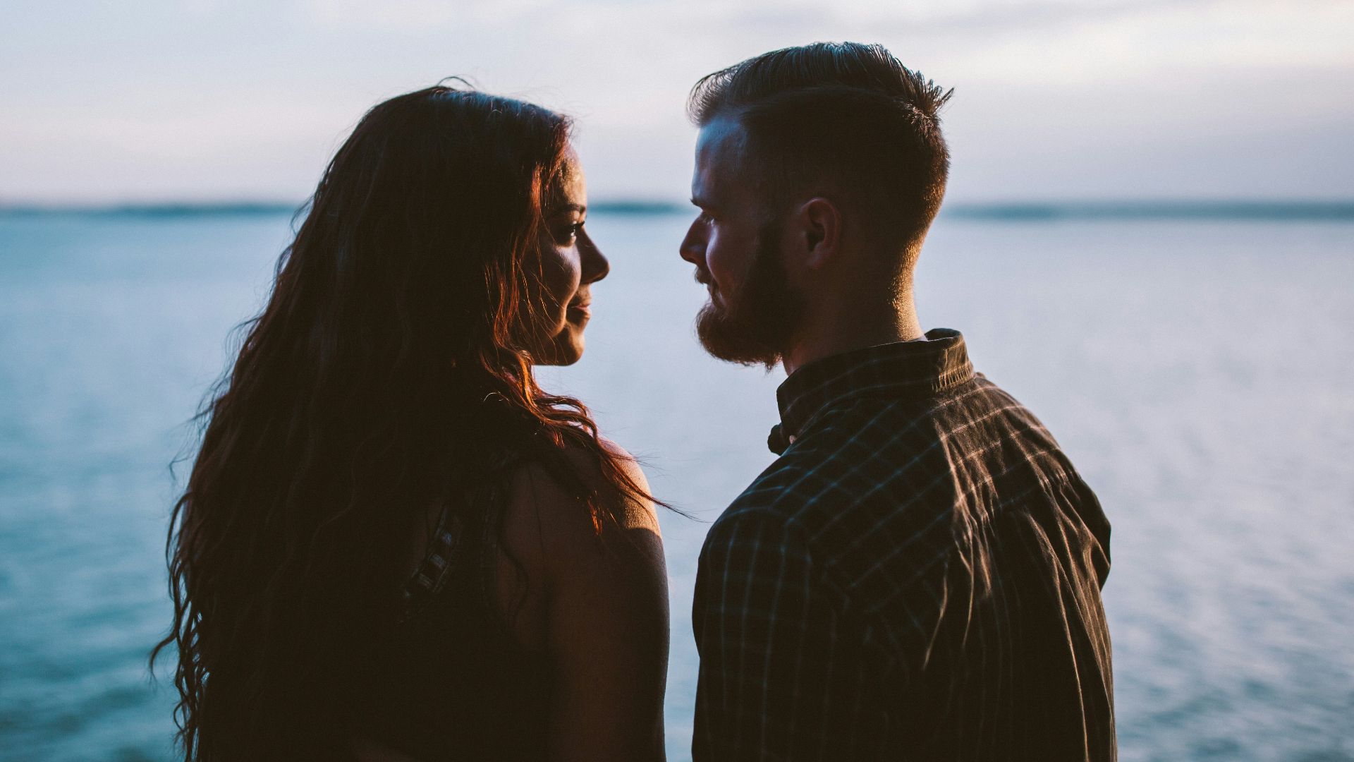 man and woman standing while looking each other near body of water