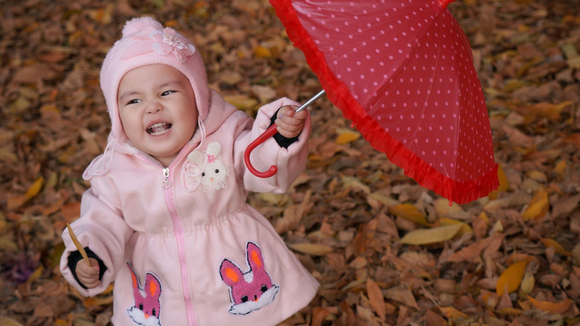 a little girl in a pink coat holding a red umbrella