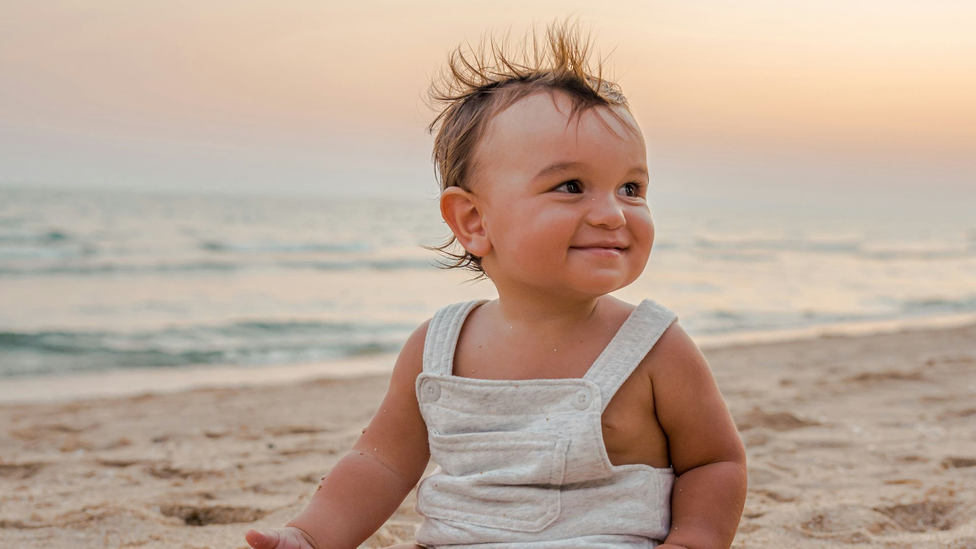 a baby sitting in the sand at the beach