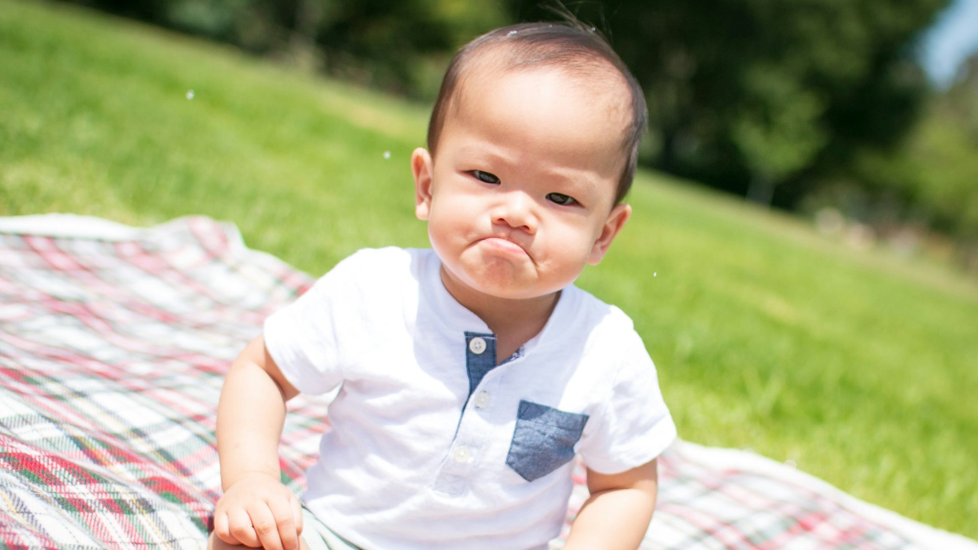 selective focus photography of grumpy face toddler sitting on plaid pad taken during daytime