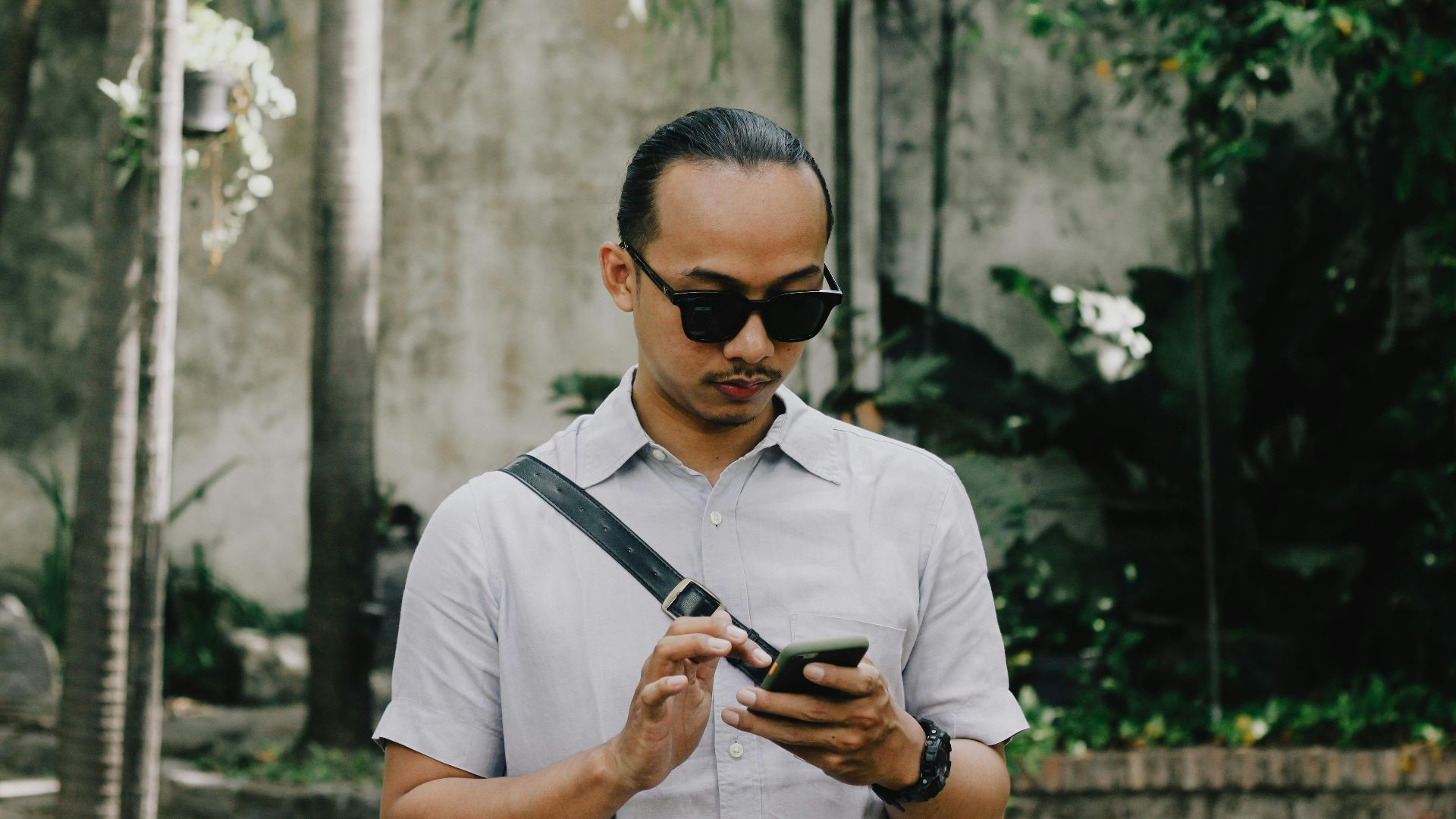 man in white button up shirt wearing black sunglasses holding black smartphone