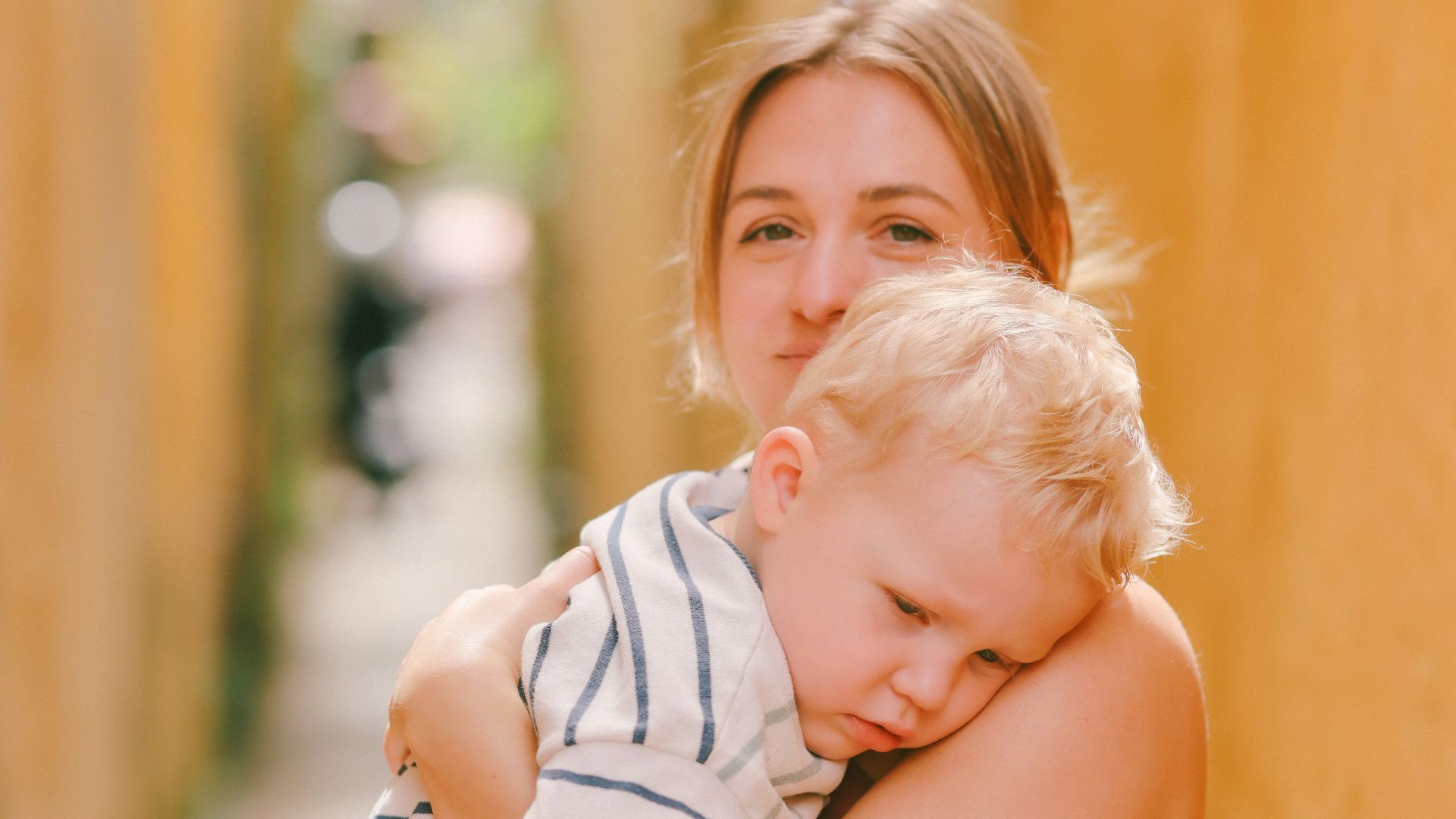 Woman holding a sleeping child in a narrow alley.