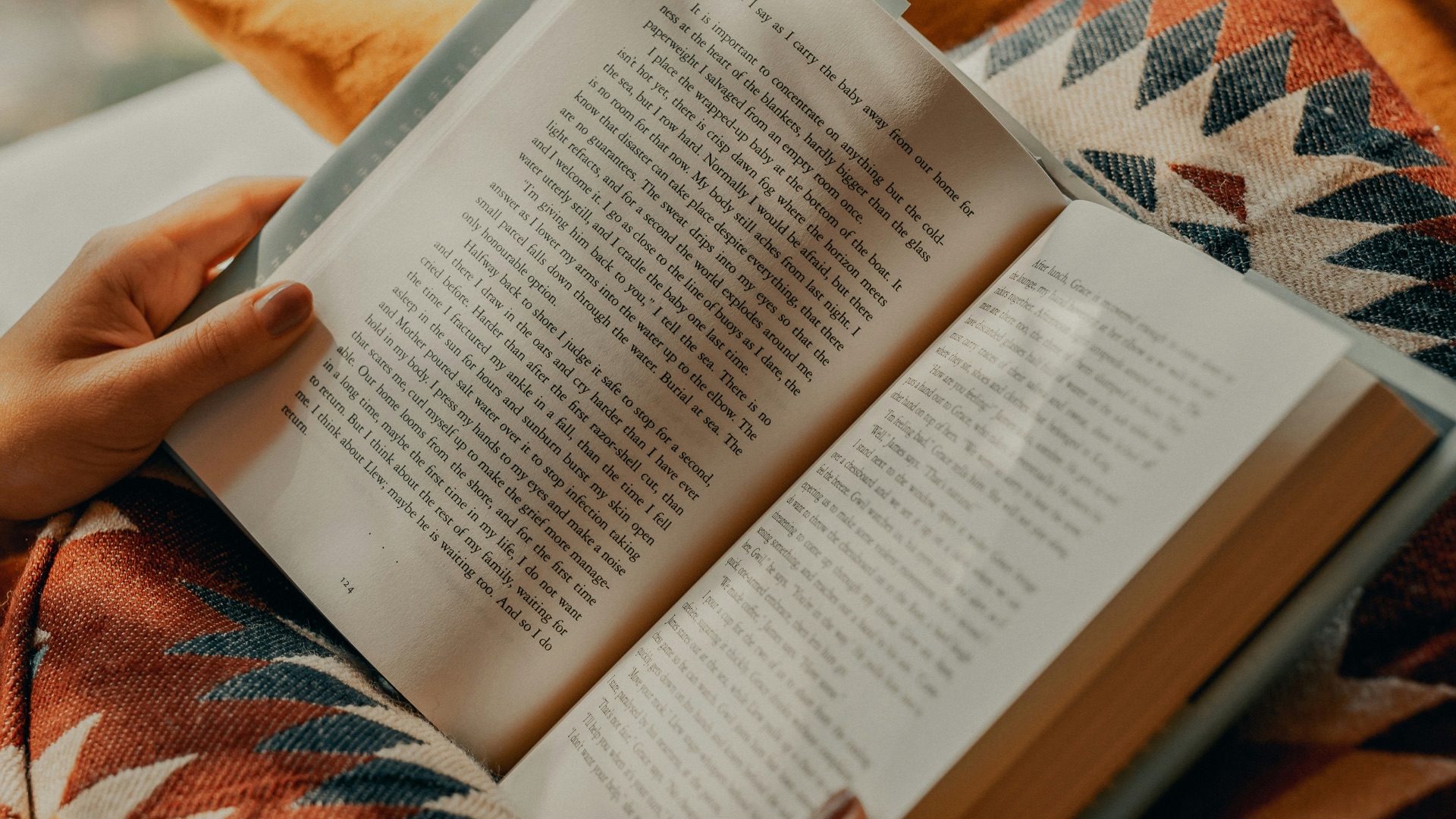 person reading book on brown and beige textile