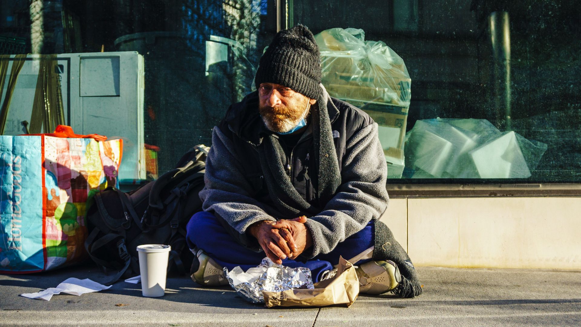 man in black and gray jacket sitting on sidewalk during daytime