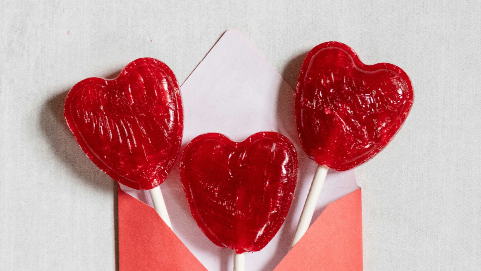 two heart shaped lollipops sticking out of an envelope