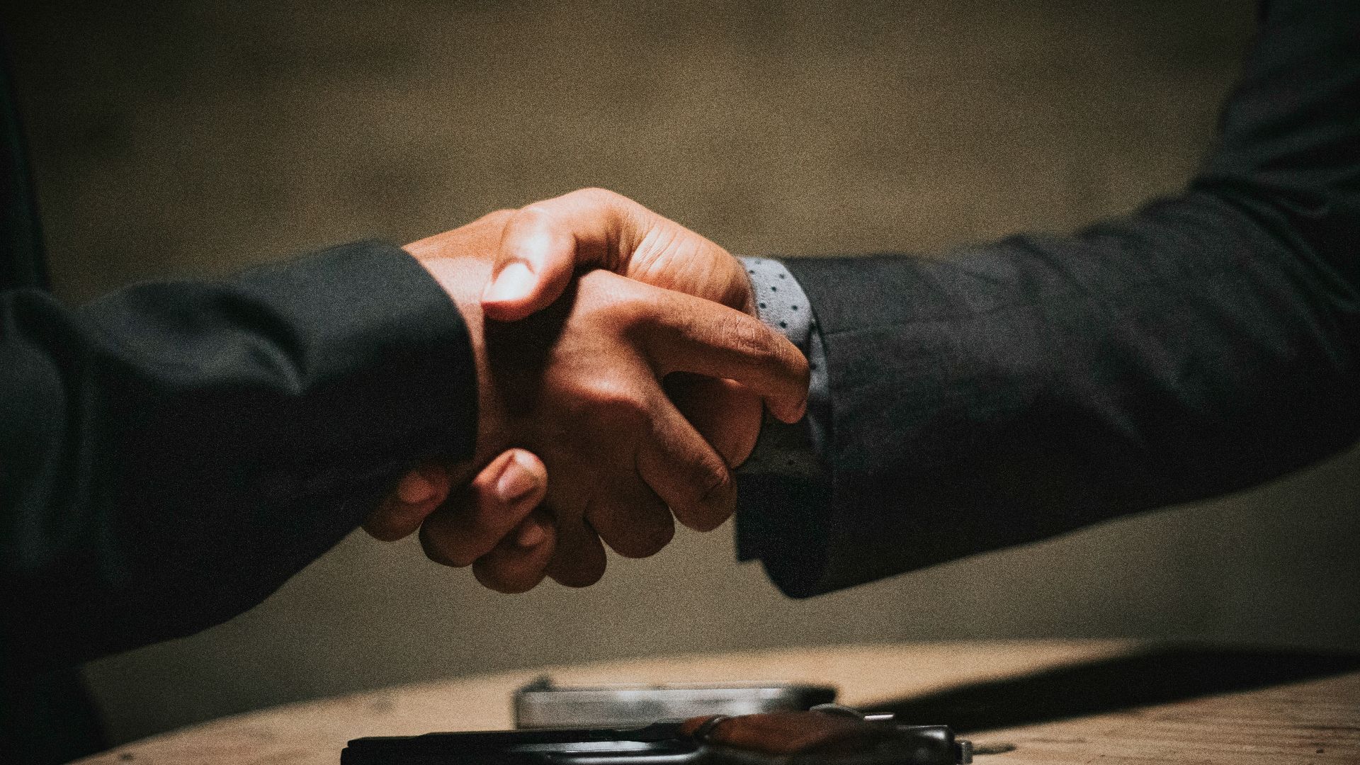 two people shaking hands over a wooden table