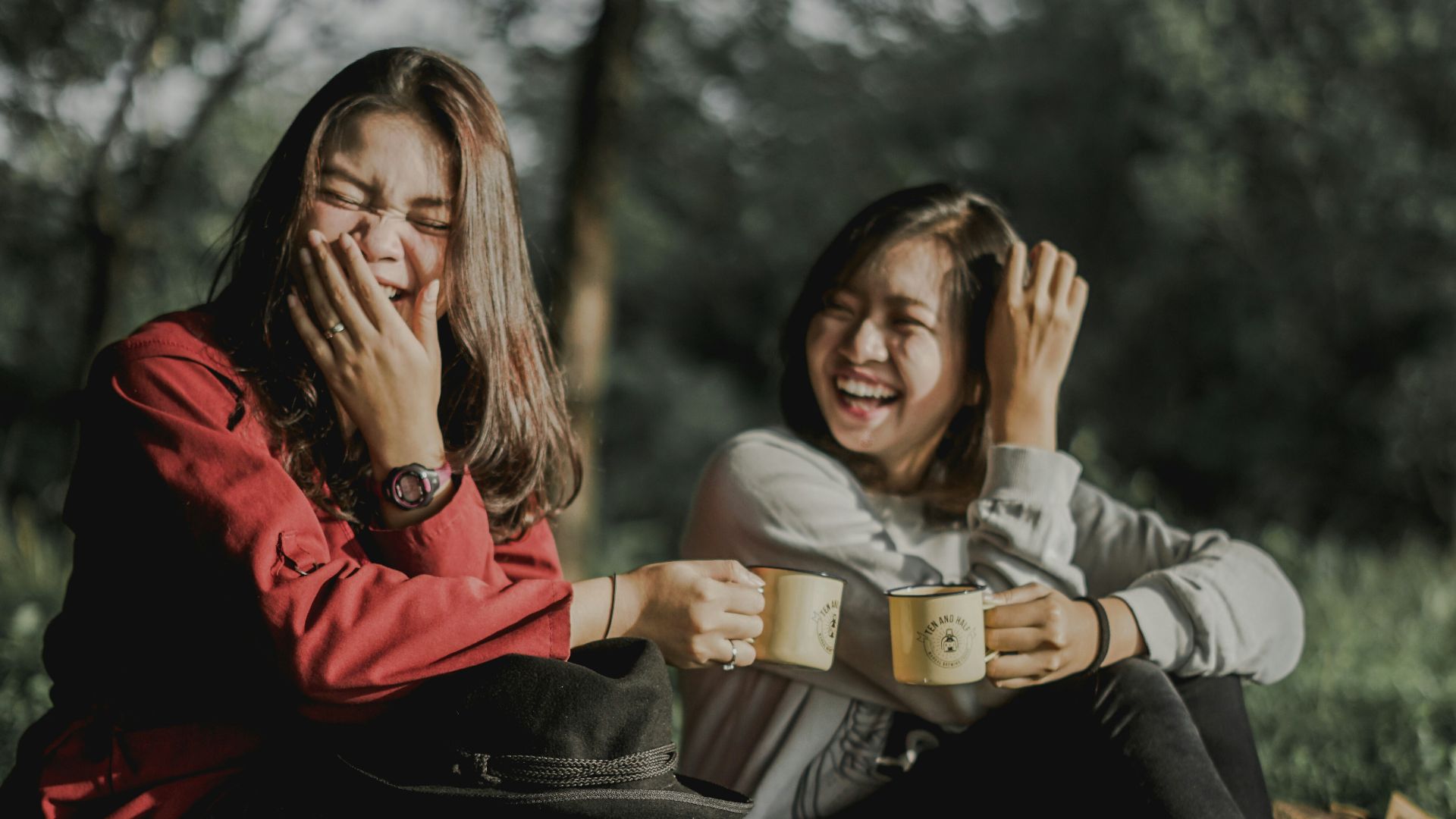 two women holding cups laughing at each other