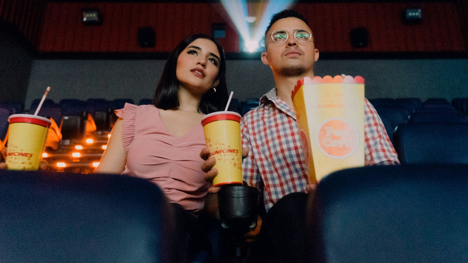 2 women sitting on blue leather chair holding white and red plastic cups